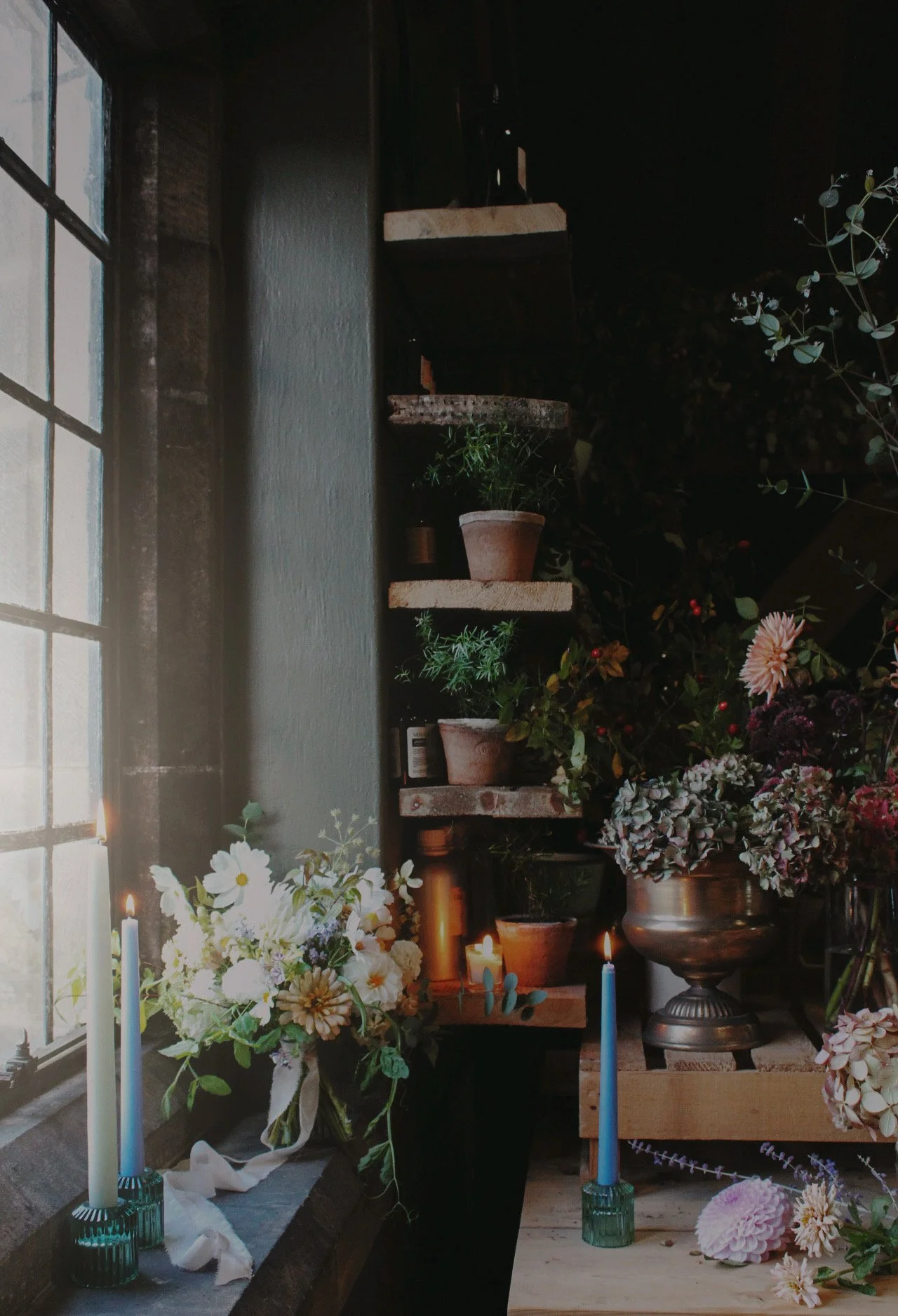 Arrangement of a wedding bridal bouquet flowers and candles by a window with a brick wall, decorated with foliage and illuminated by candles.