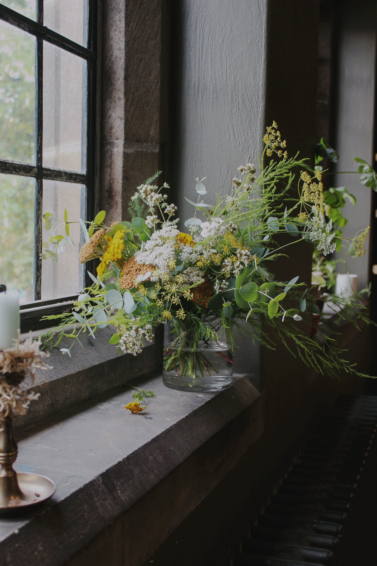 Low glass banquet vase filled with an abundant arrangement of seasonal flowers, foliage and delicate white and yellow blooms.