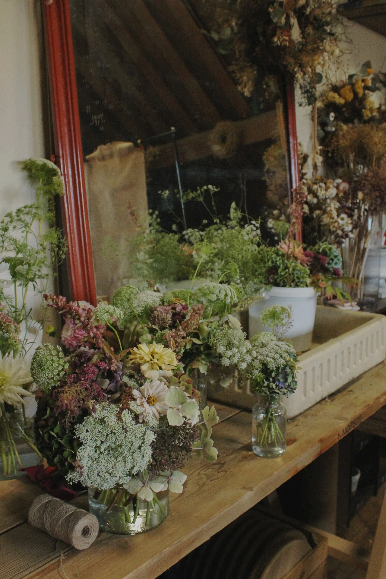 Autumn flowers and foliage arranged in glass vases on a wooden potting bench at The Wild Potager Co.