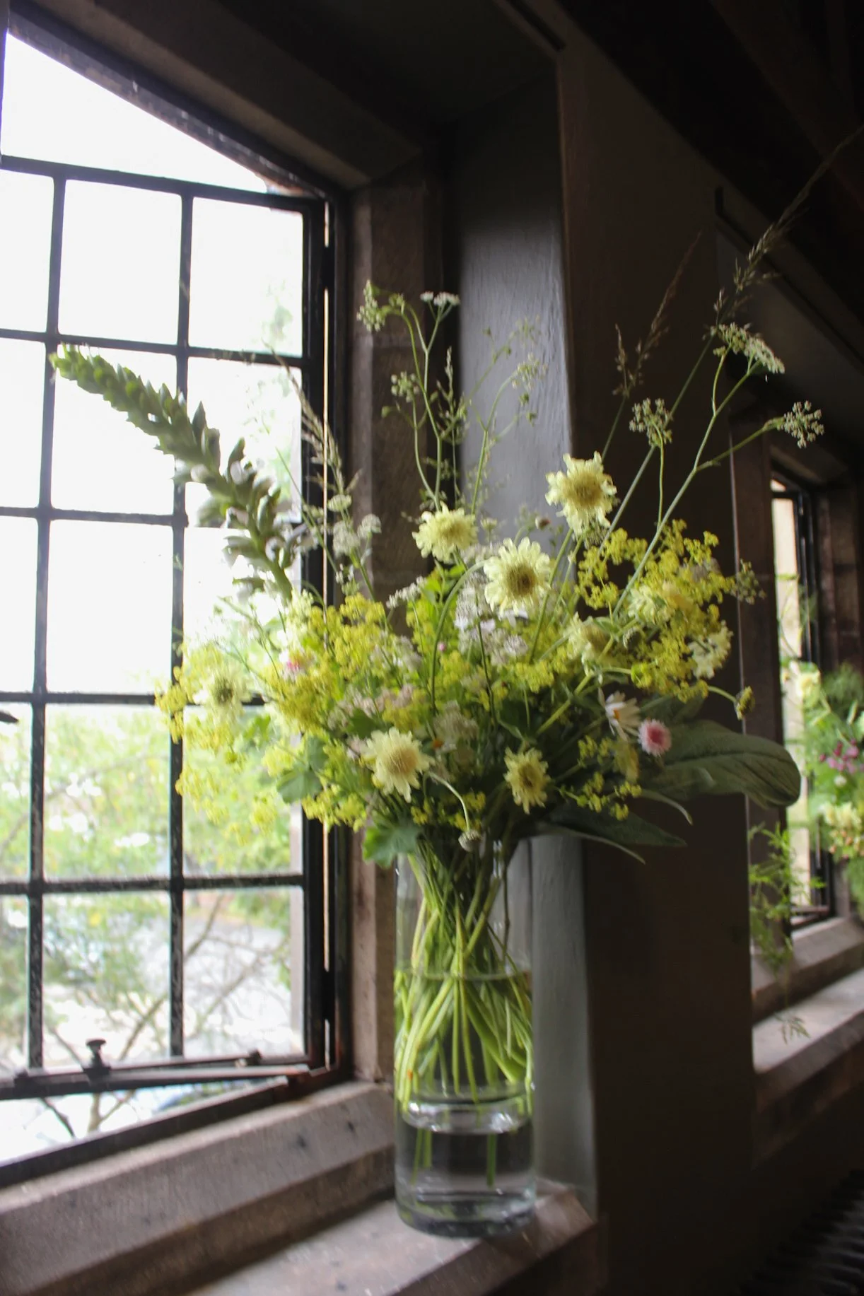 Signature Statement Centrepiece featuring soft seasonal blooms and generous foliage in a glass vessel, creating an elegant wedding display.