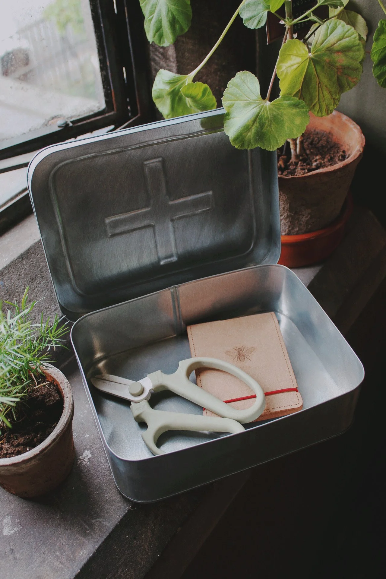 Galvanised Potager Rescue Tin with red cross, shown among potted flowers and garden plants.