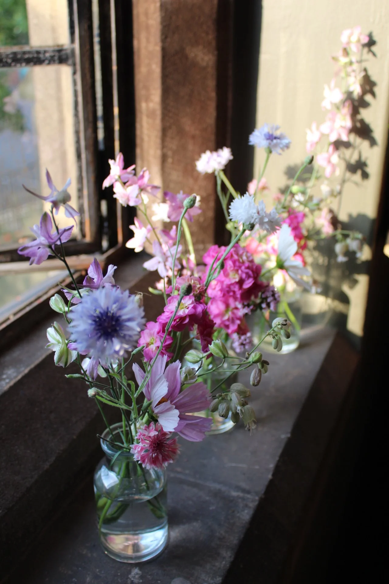 Large glass bud vase filled with colourful seasonal wedding flowers beside a window.