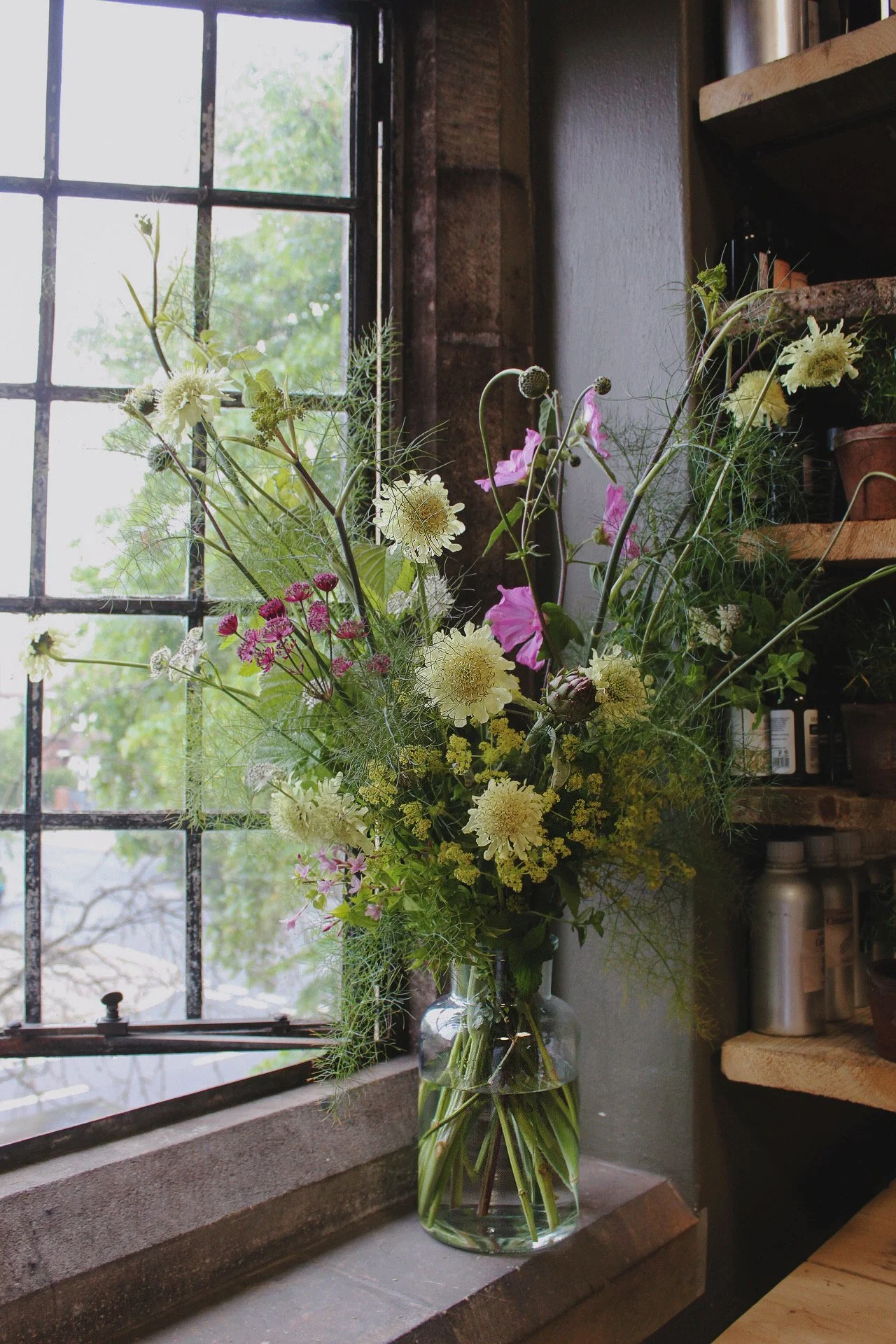 Signature Statement Centrepiece arranged with abundant seasonal flowers, airy foliage and natural movement beside a window.
