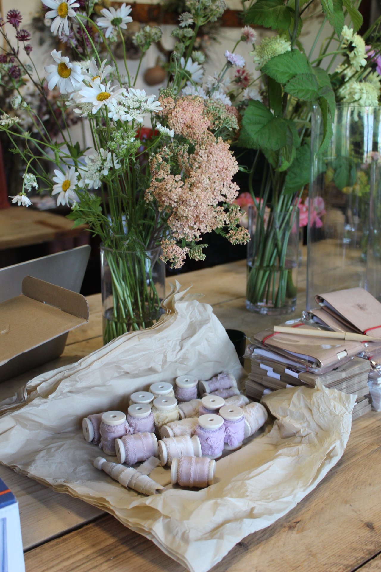 Rolls of silk ribbon beside seasonal flowers on the studio workbench.