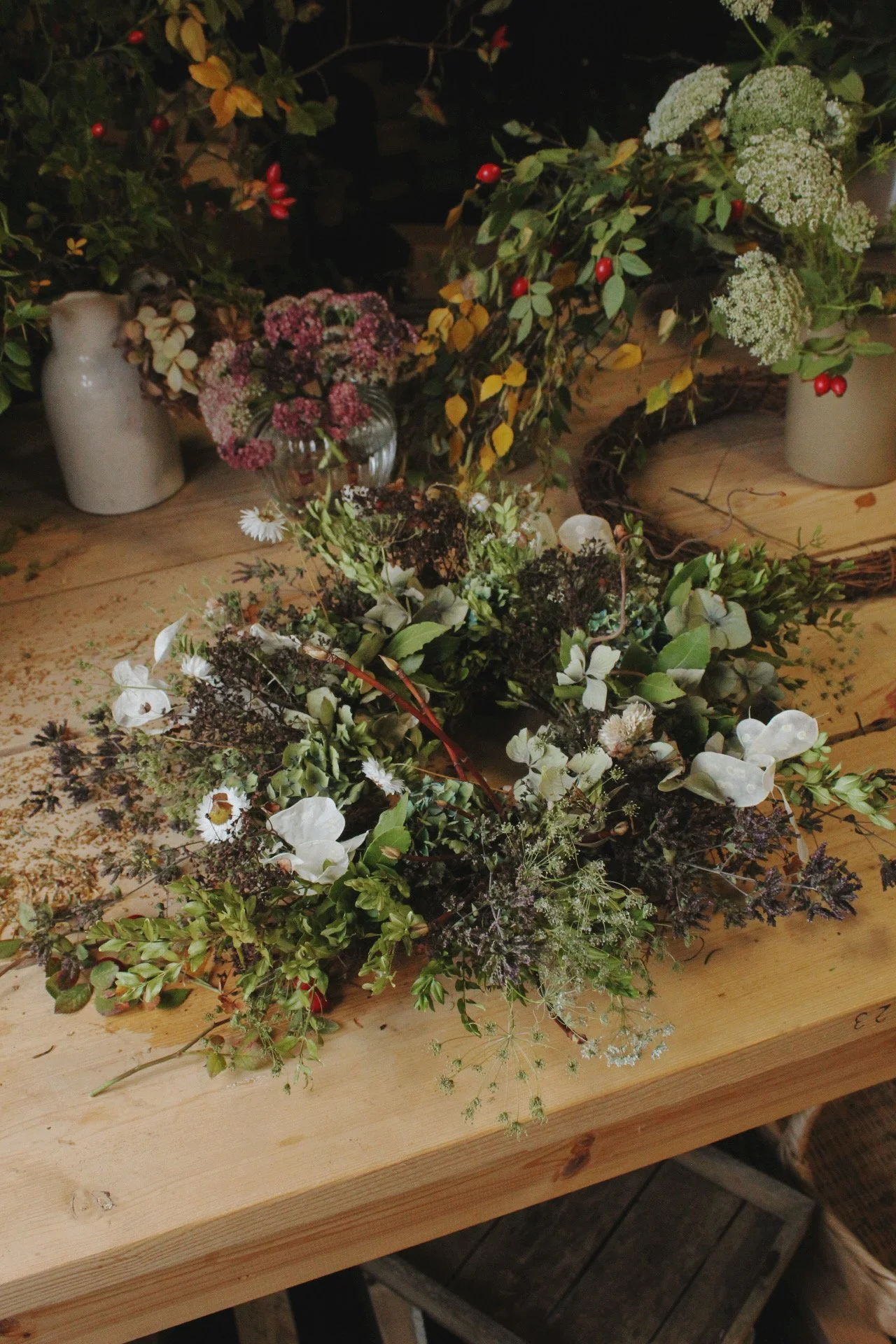 Flowers, foliage and a handmade wreath arranged on the worktable in The Wild Potager Co studio.