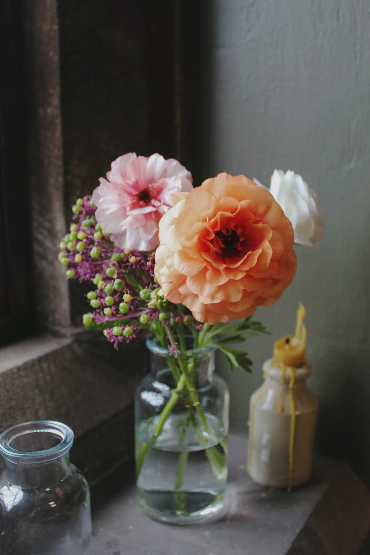 Large glass bud vase filled with a loose, colourful arrangement of seasonal flowers on a stone windowsill.