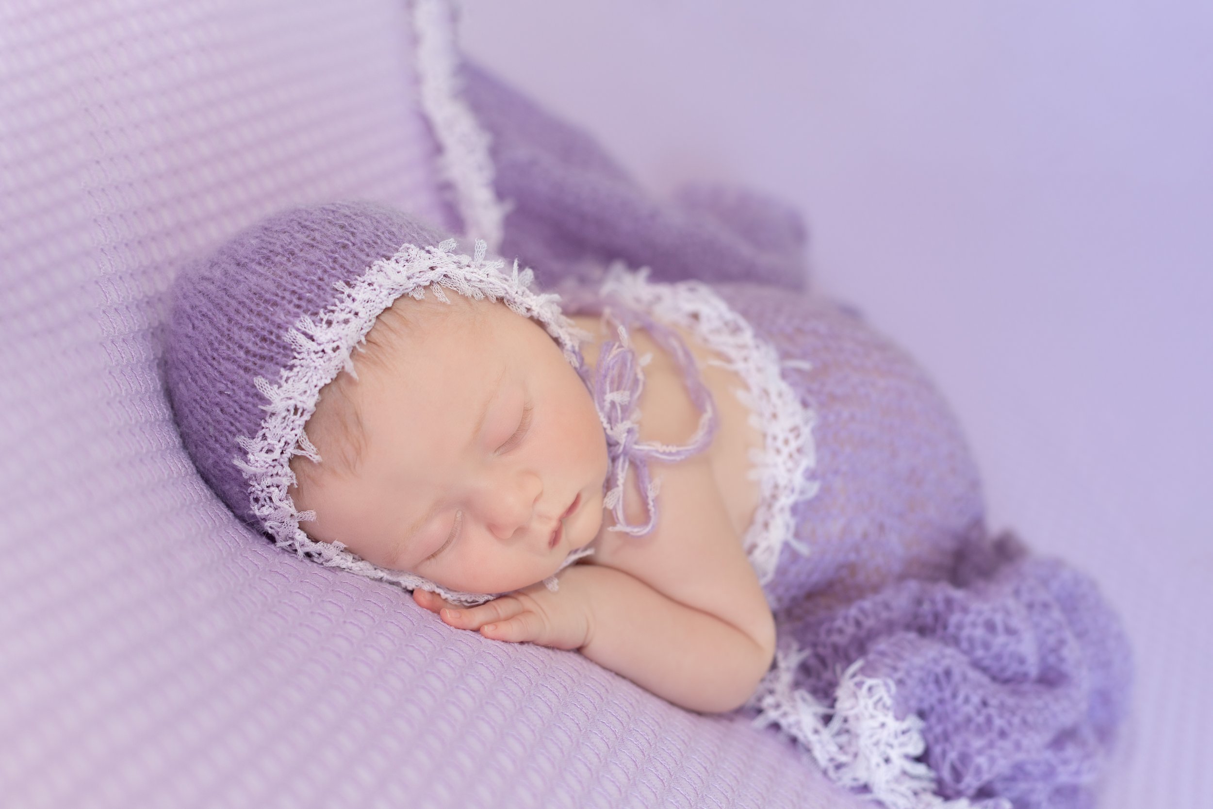 newborn baby girl with a mauve purple bonnet and blanket wrap