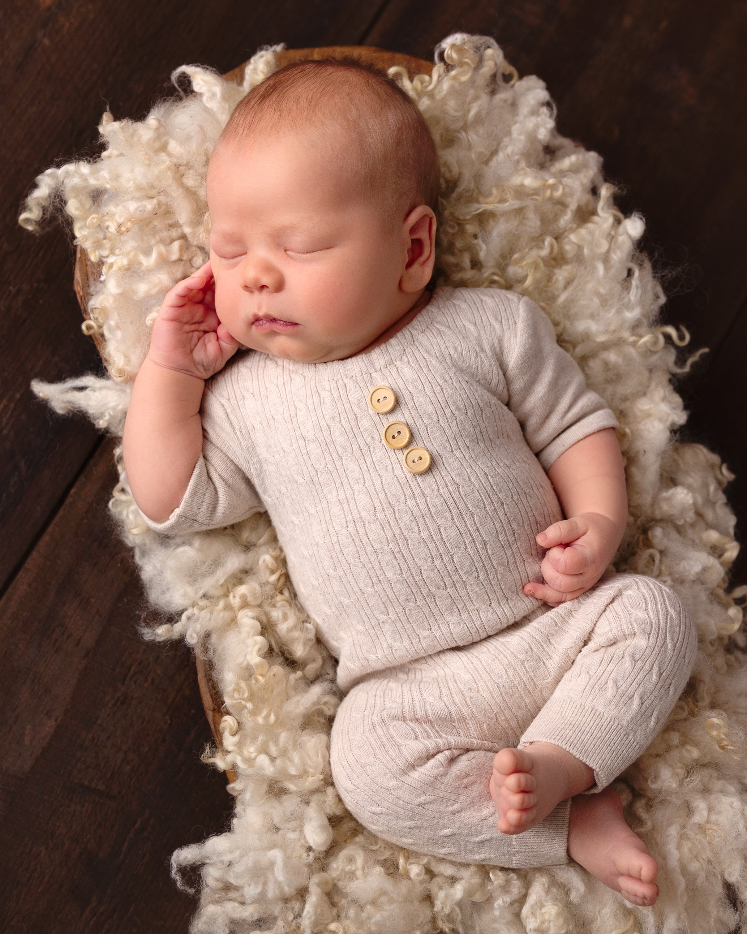 newborn wearing beige romper in a brown basket