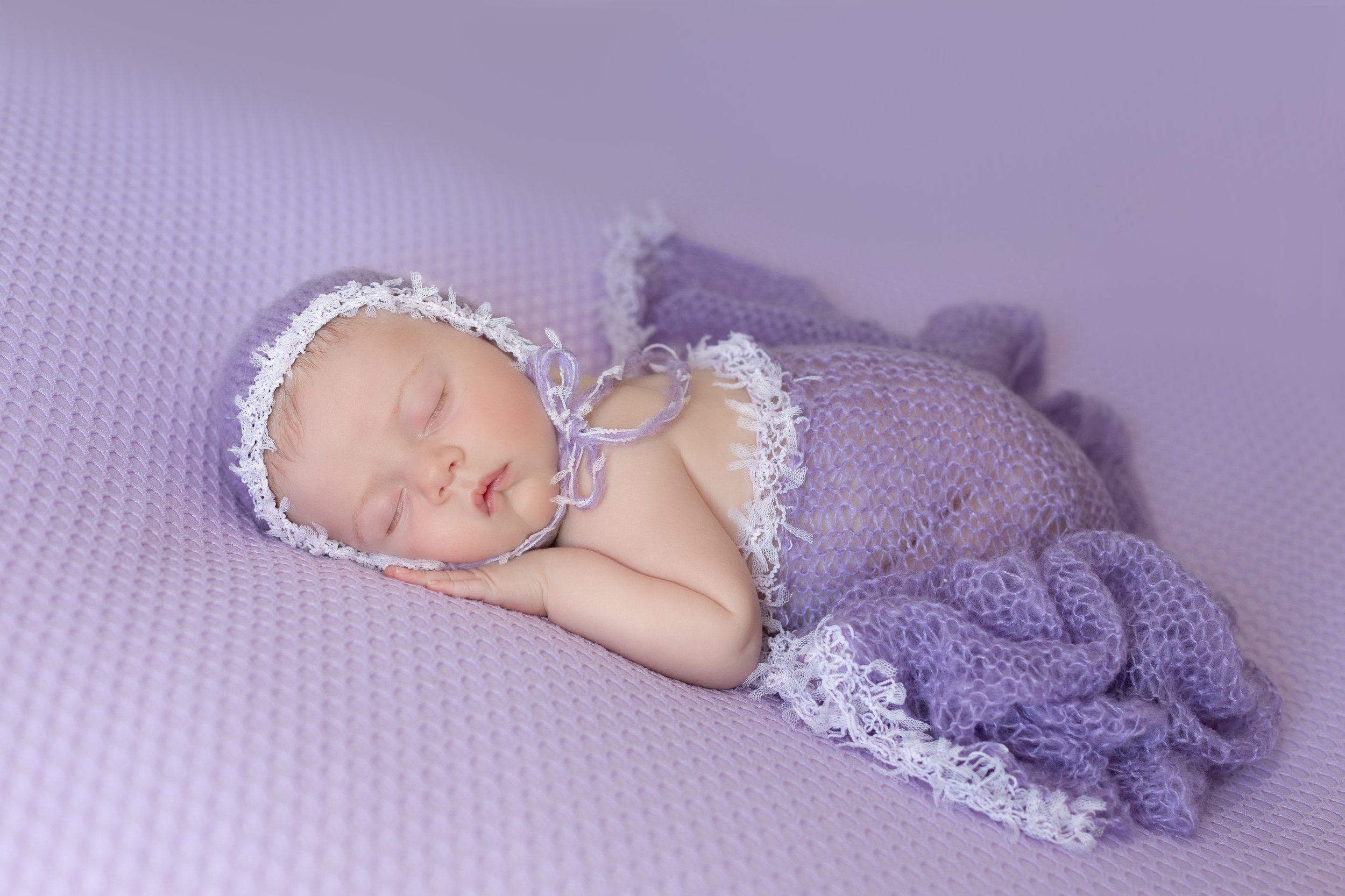 baby photo of girl wearing frilly bonnet covered in a blanket