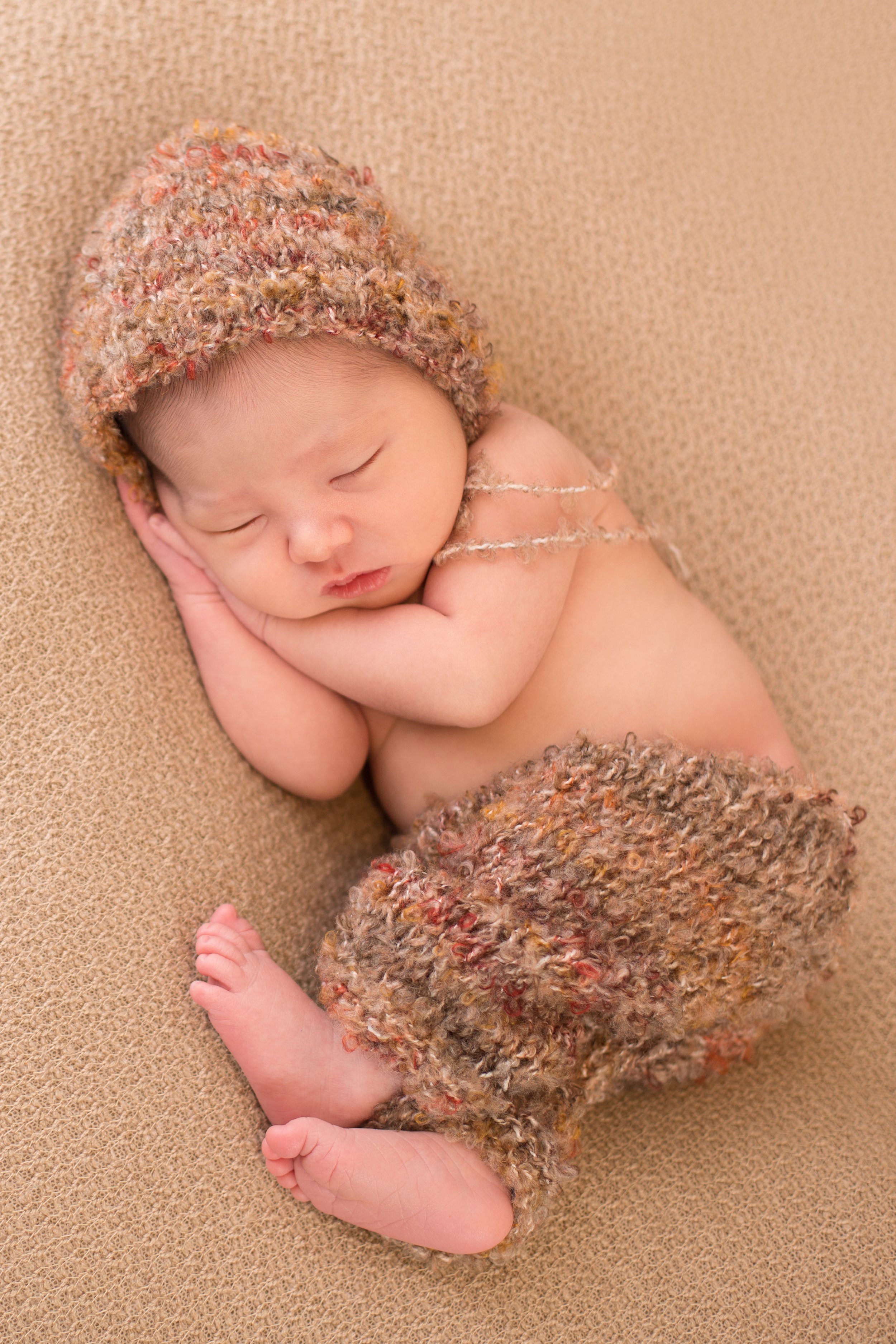 sleeping baby boy in autumn coloured pants and bonnet