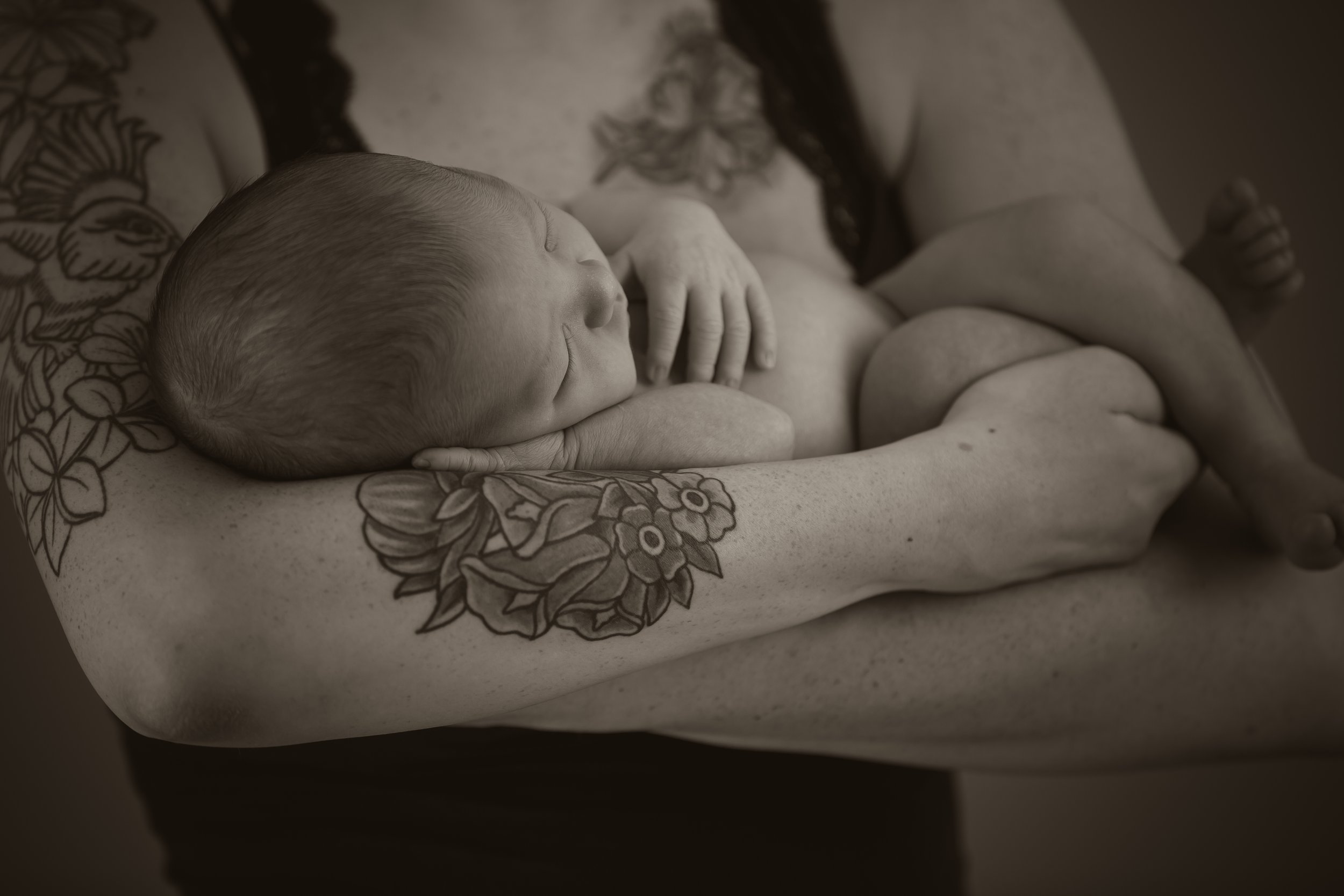 black and white image of tattooed mom cradling baby in arms