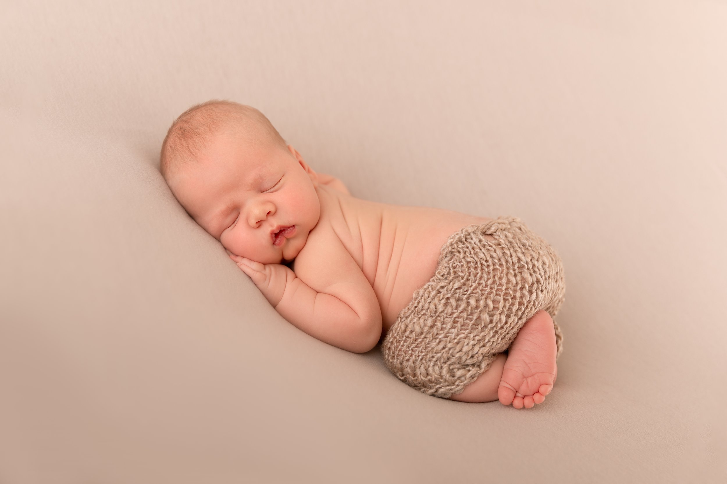 newborn boy in beige hand knit pants in bum up pose