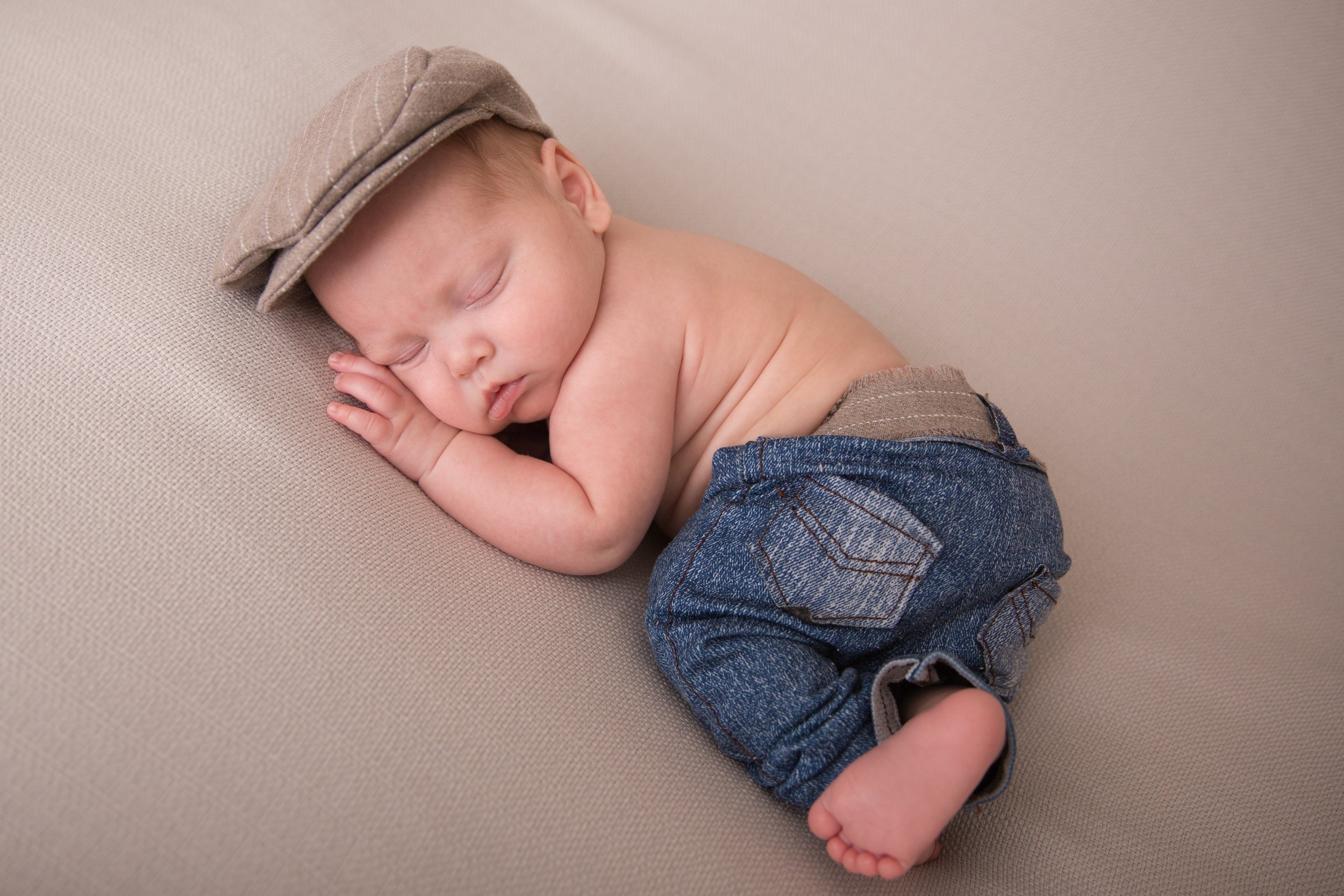 newborn boy wearing cap and jeans on newborn posing bag