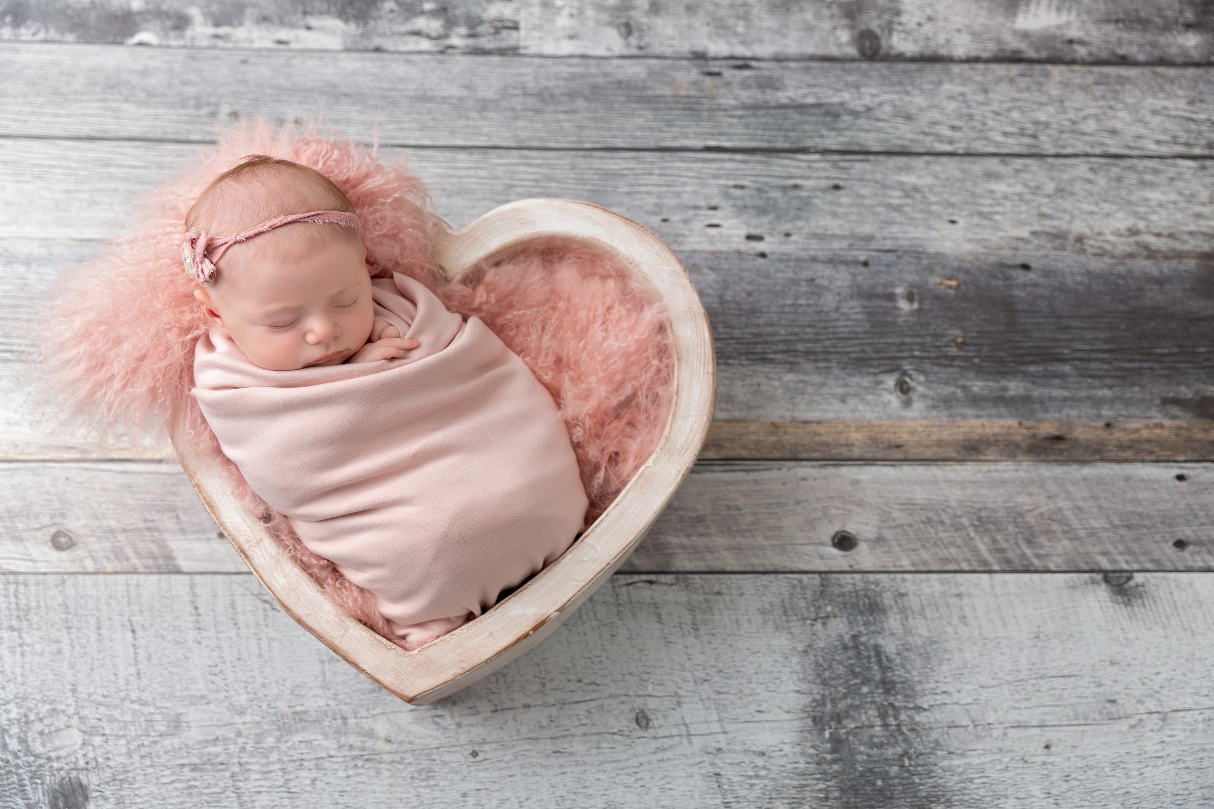 swaddled baby girl in wooden heart bowl