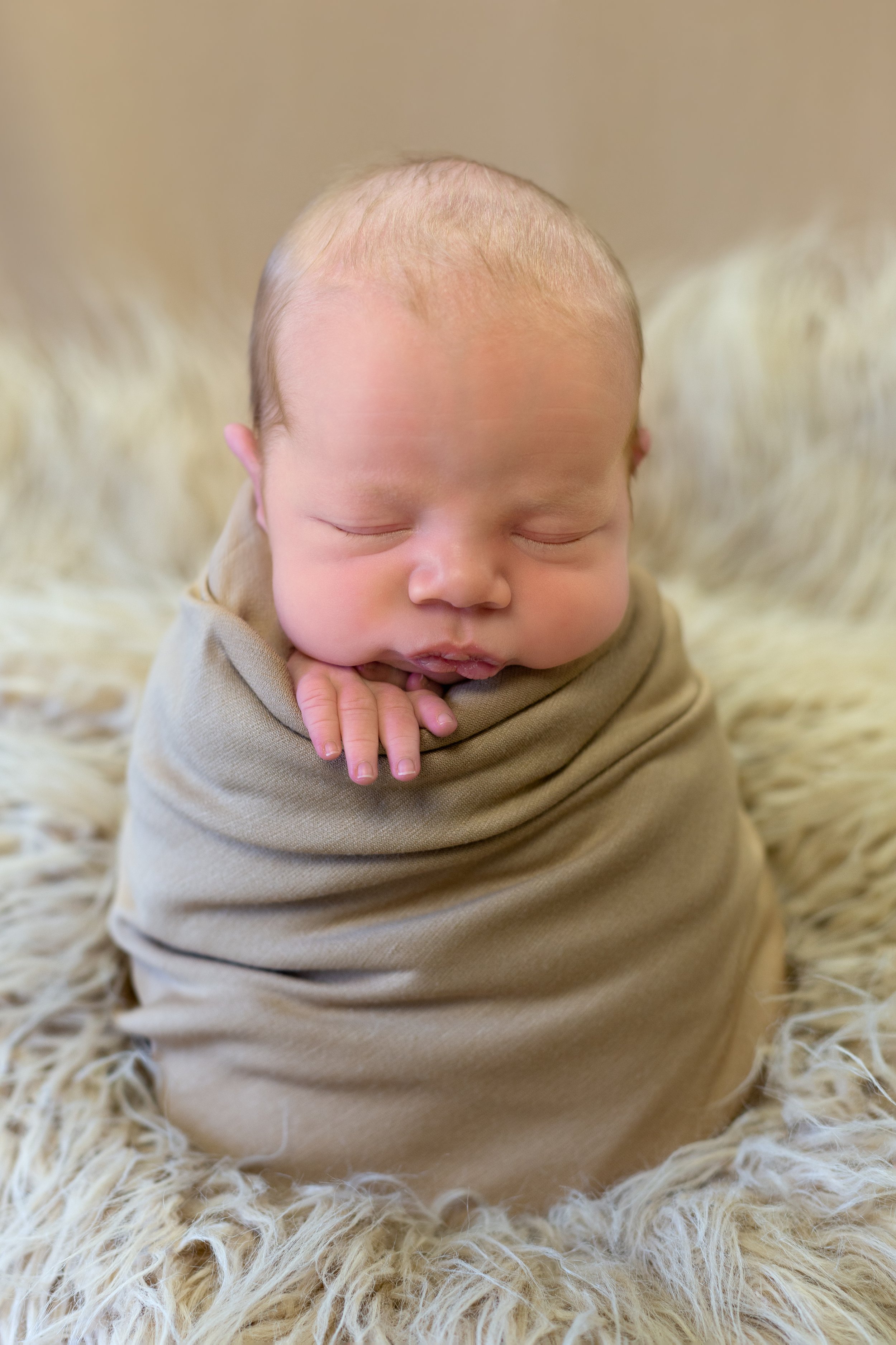 boy swaddled in beige in newborn potato sack pose