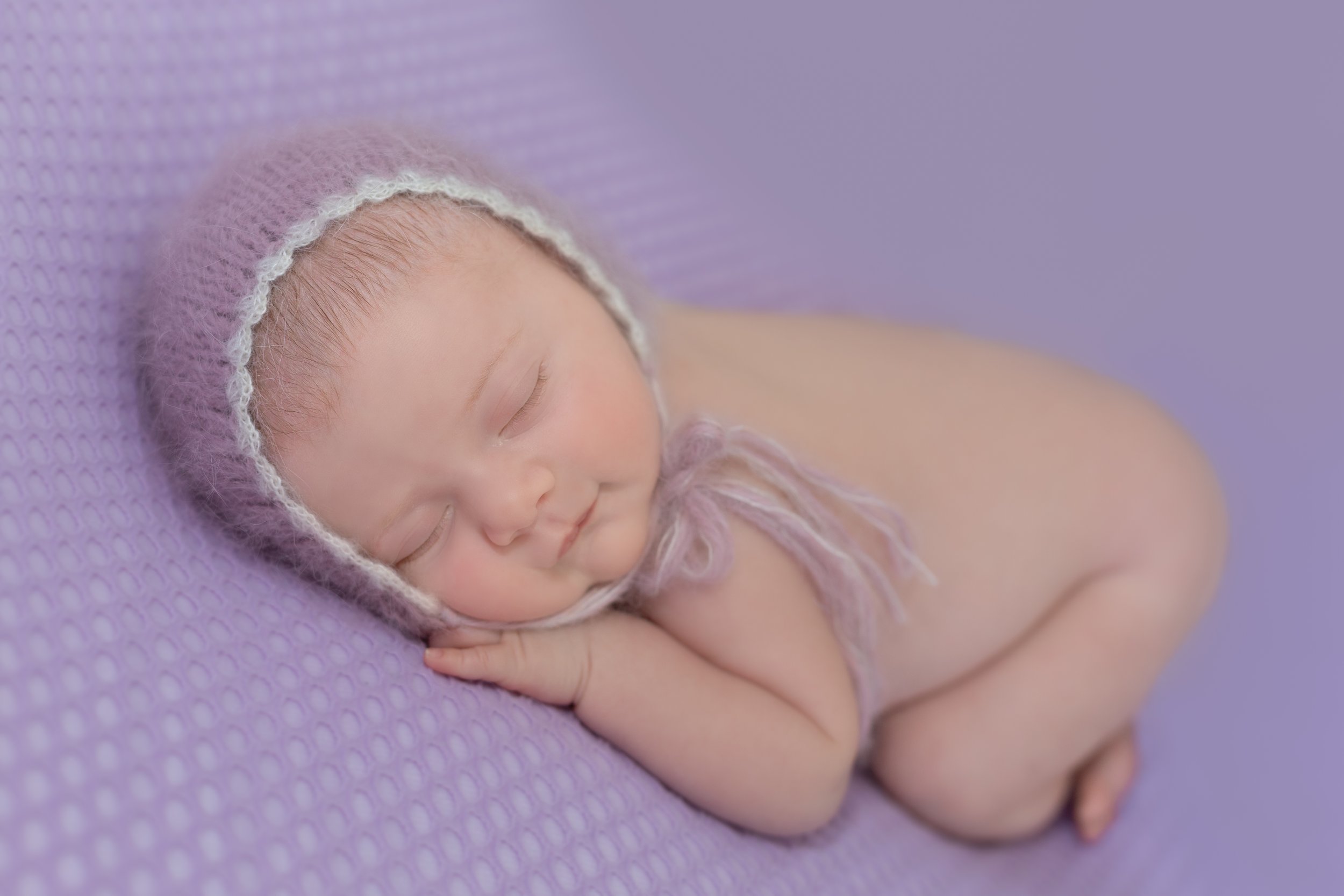 newborn baby girl wearing embellished bonnet on purple blanket