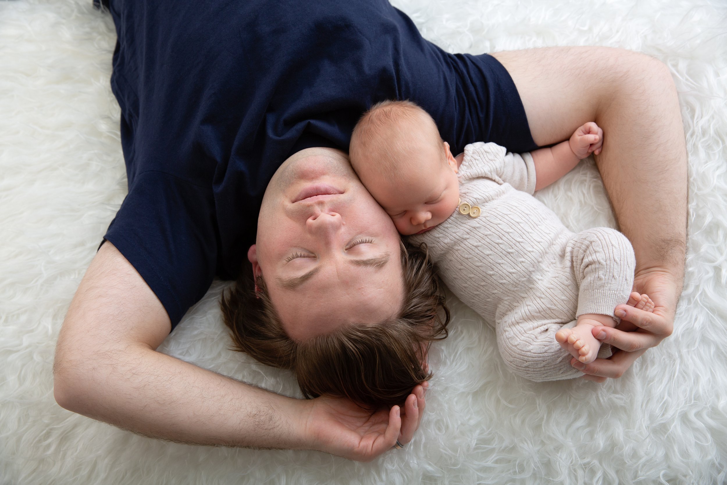 dad and newborn son lying on white flokati rug