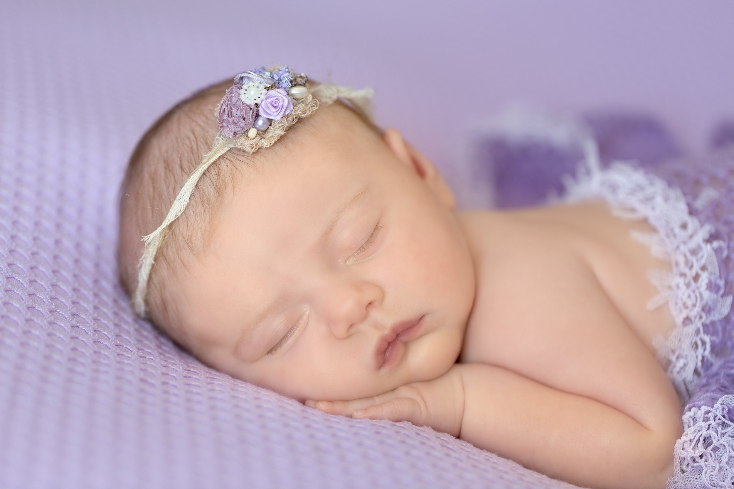 newborn baby girl on purple blanket wearing pretty headband