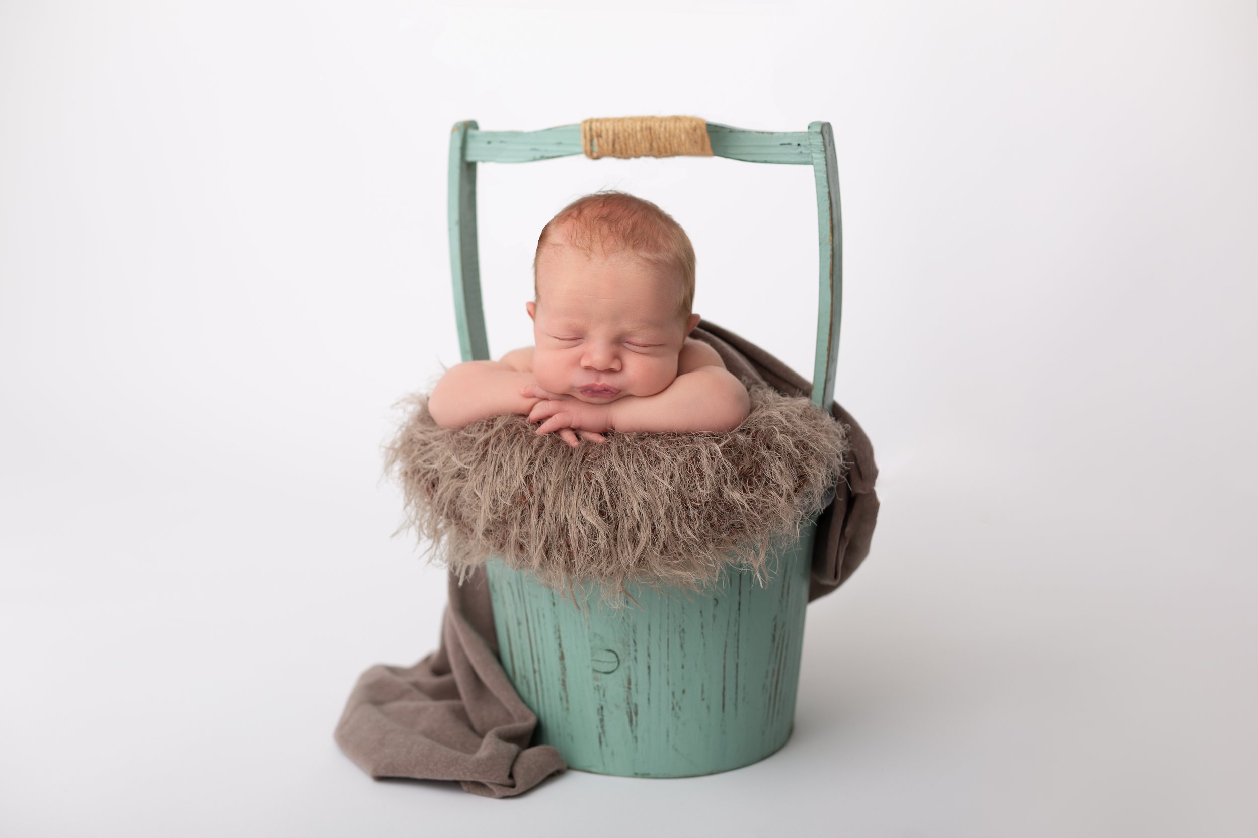 newborn posed chin on hands in teal coloured bucket