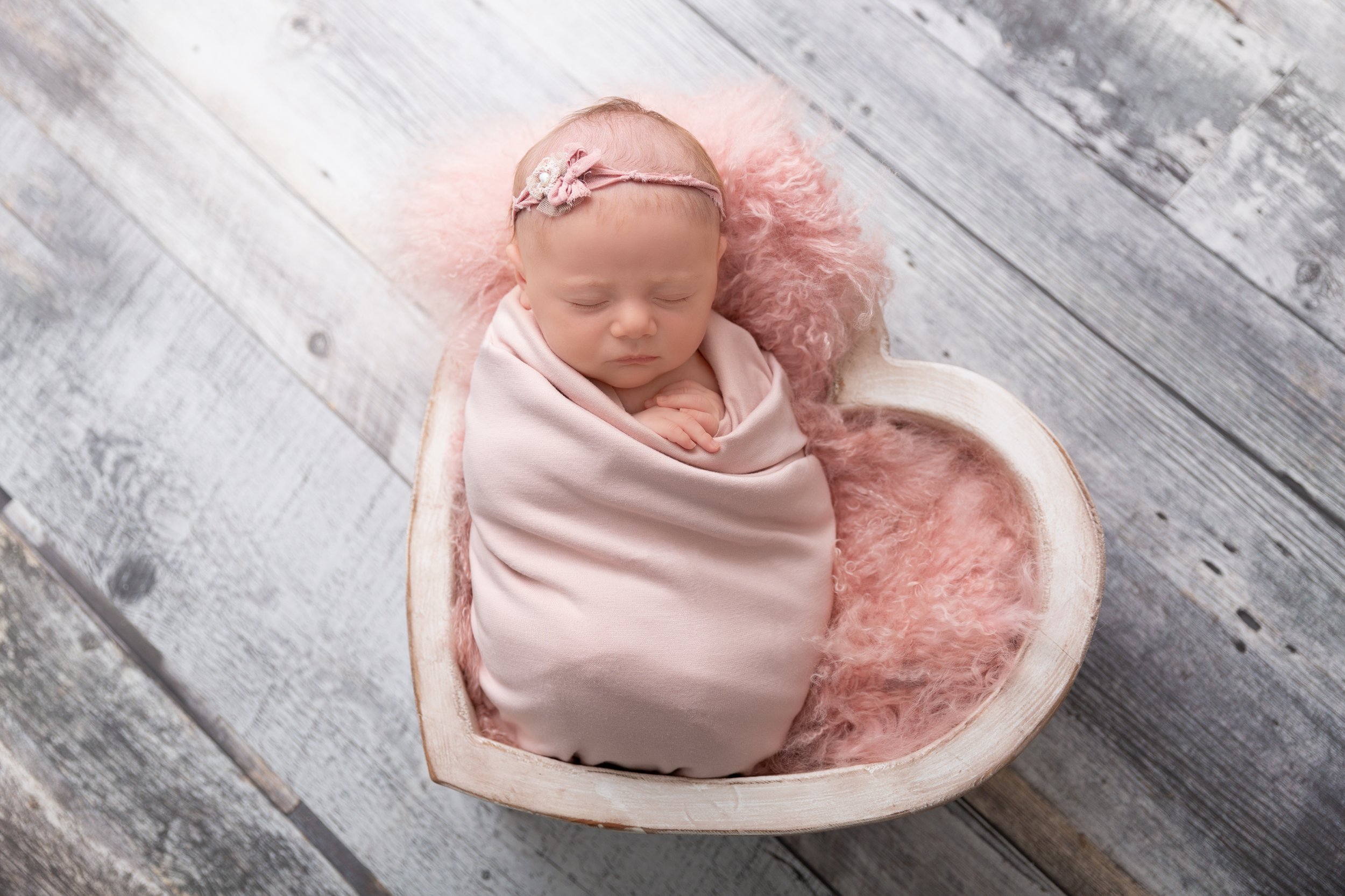 swaddled baby girl posed in a wooden heart bowl