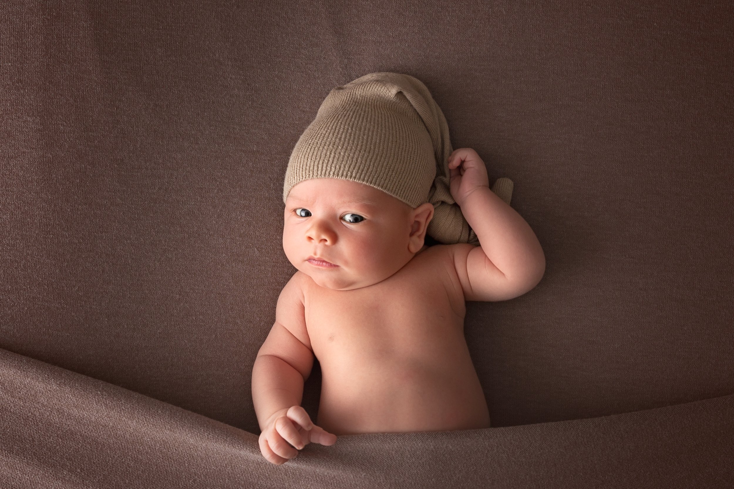 awake baby with sleepy cap tucked into a brown blanket