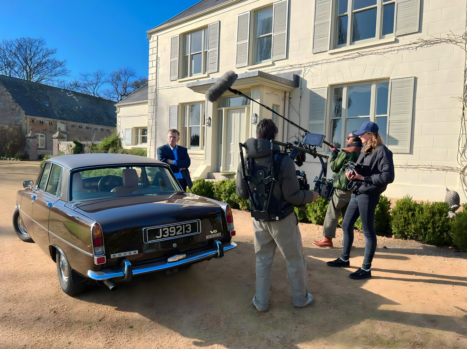Eloise Singer directing crew with actor beside classic black Rover outside white house during  shoot with Tim Cragg, Emmy winning Cameramn