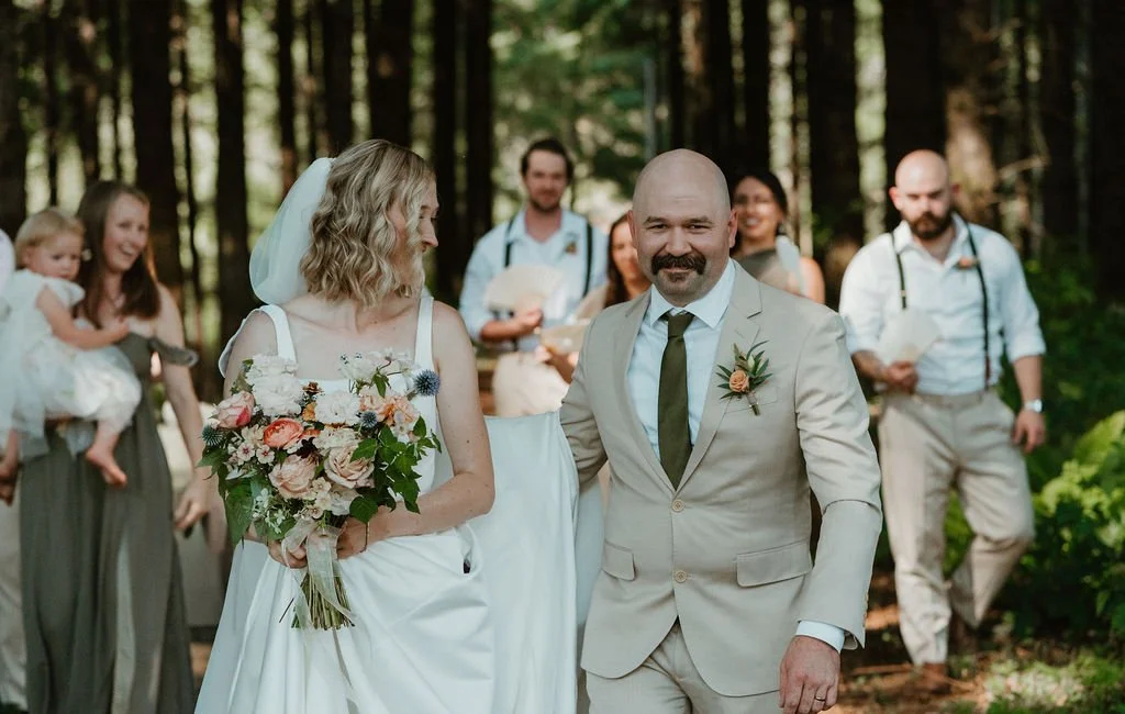 Bride and groom walking down a forest aisle after their ceremony at Riverbend Orchard, surrounded by wedding guests.