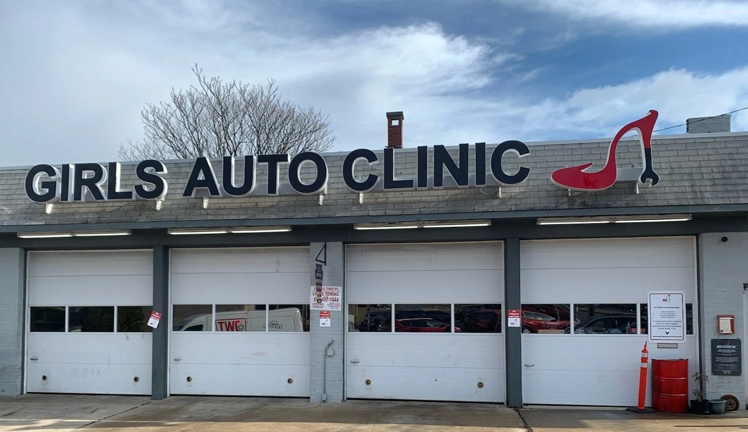 Exterior of a building with a sign reading 'Girls Auto Clinic' and a red high-heeled shoe logo.
