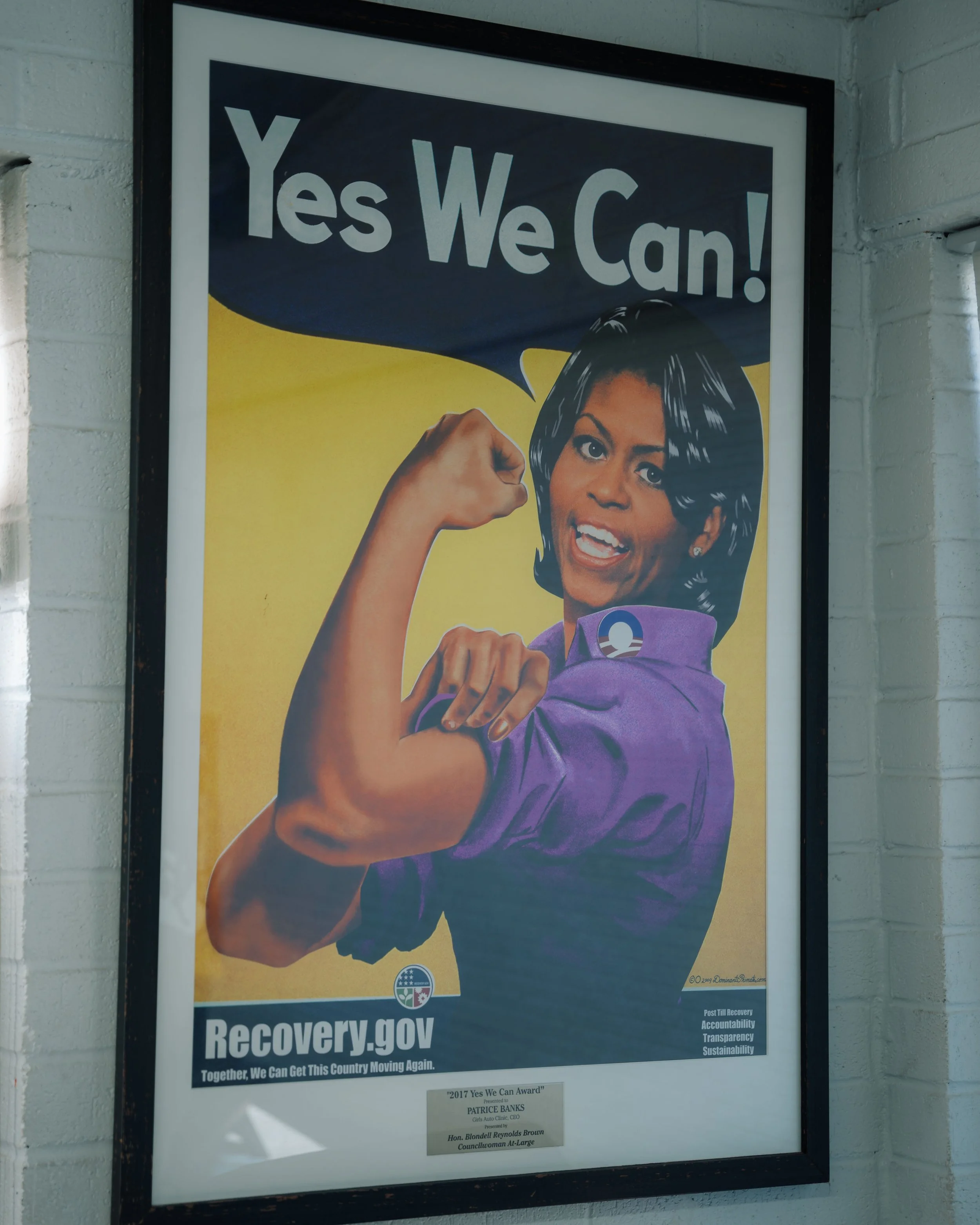 A poster inspired by 'Rosie the Riveter' featuring an African American woman wearing a purple shirt and showing her flexed arm with the slogan 'Yes We Can!' at the top. It promotes the website recovery.gov with message about collective effort and rec