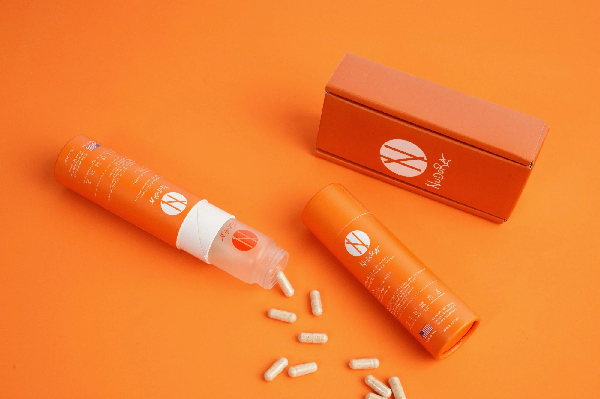 Nudora wellness supplement capsules and orange bottles on a vivid orange background