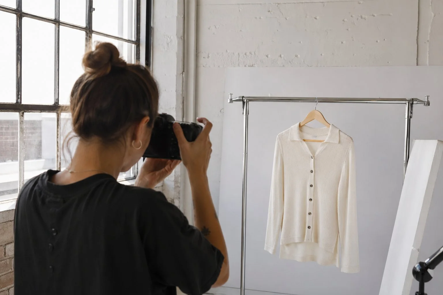 Photographer shooting a cream knit cardigan on a clothing rack in a sunlit studio, fashion product photography