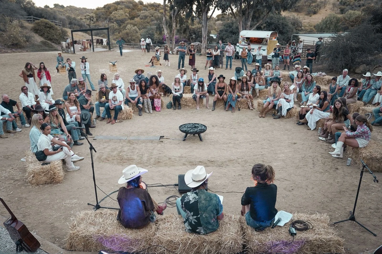 Wide view of guests gathered in a circle on hay bales around a fire pit for a panel at the Iron Rodeo Visionary event