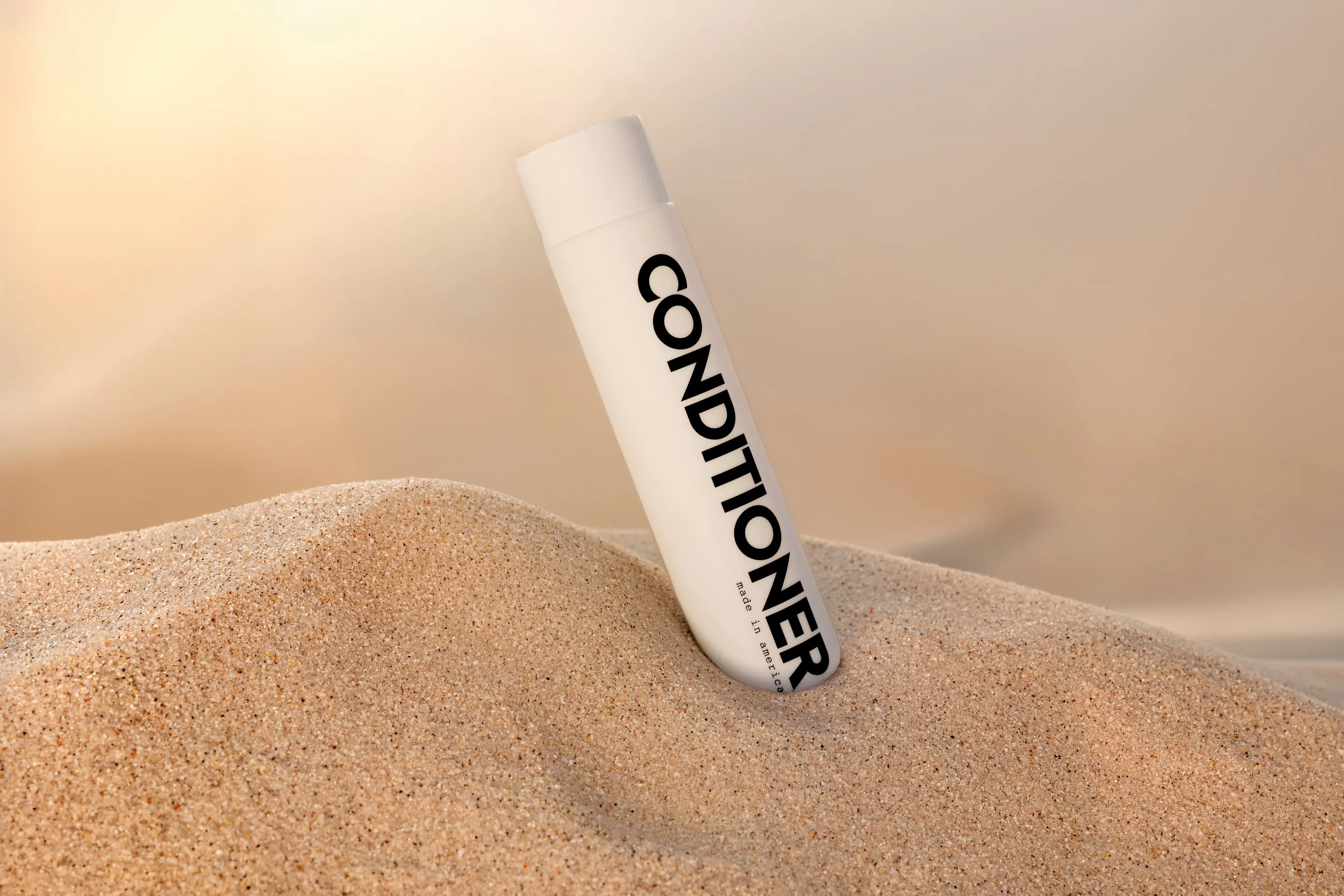 Conditioner bottle half-buried in sand dunes — haircare lifestyle product photographer Los Angeles
