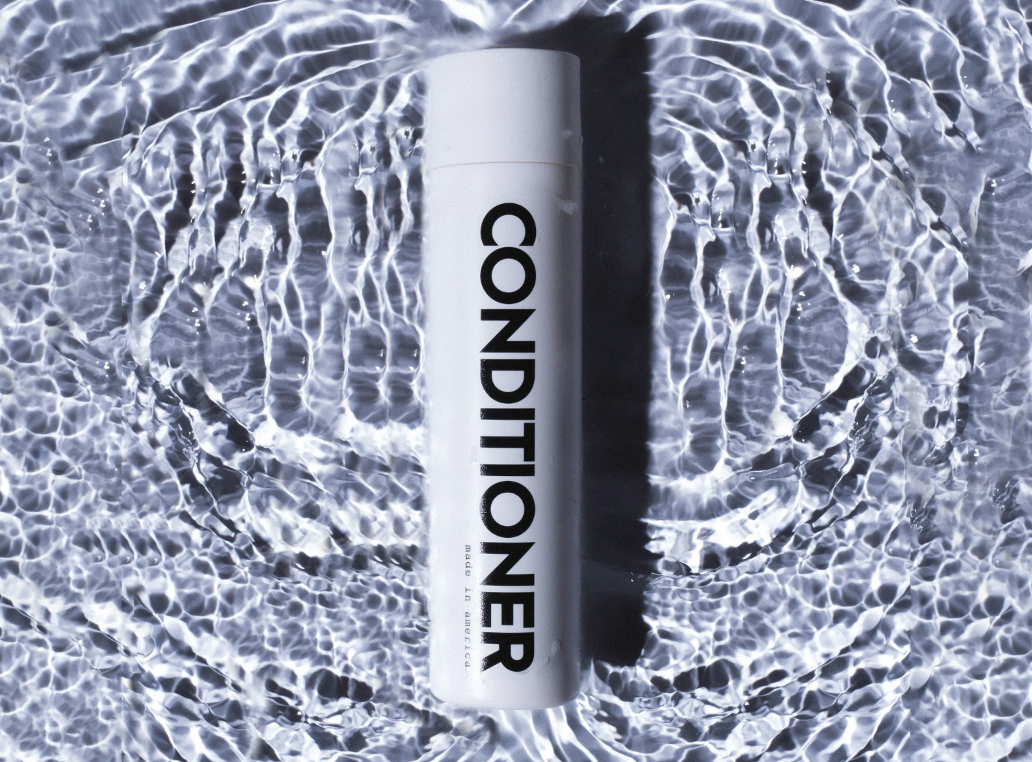 White conditioner bottle photographed in rippling water with high-contrast studio lighting