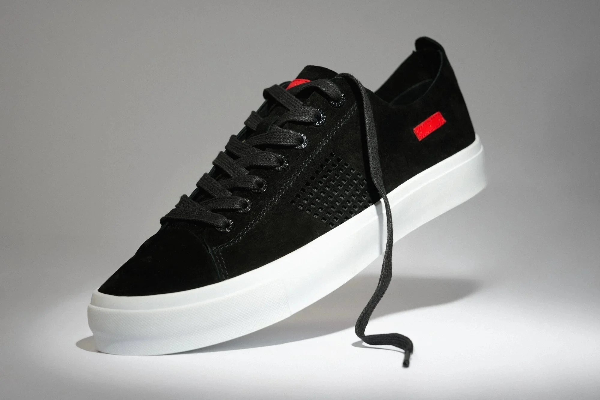 Black suede sneaker with a red tab shot in studio against a graduated gray backdrop with controlled lighting