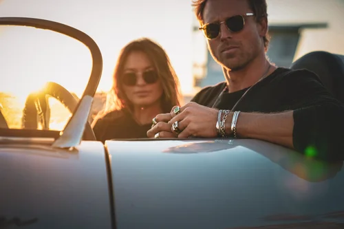 Man wearing layered silver jewelry seated in a convertible