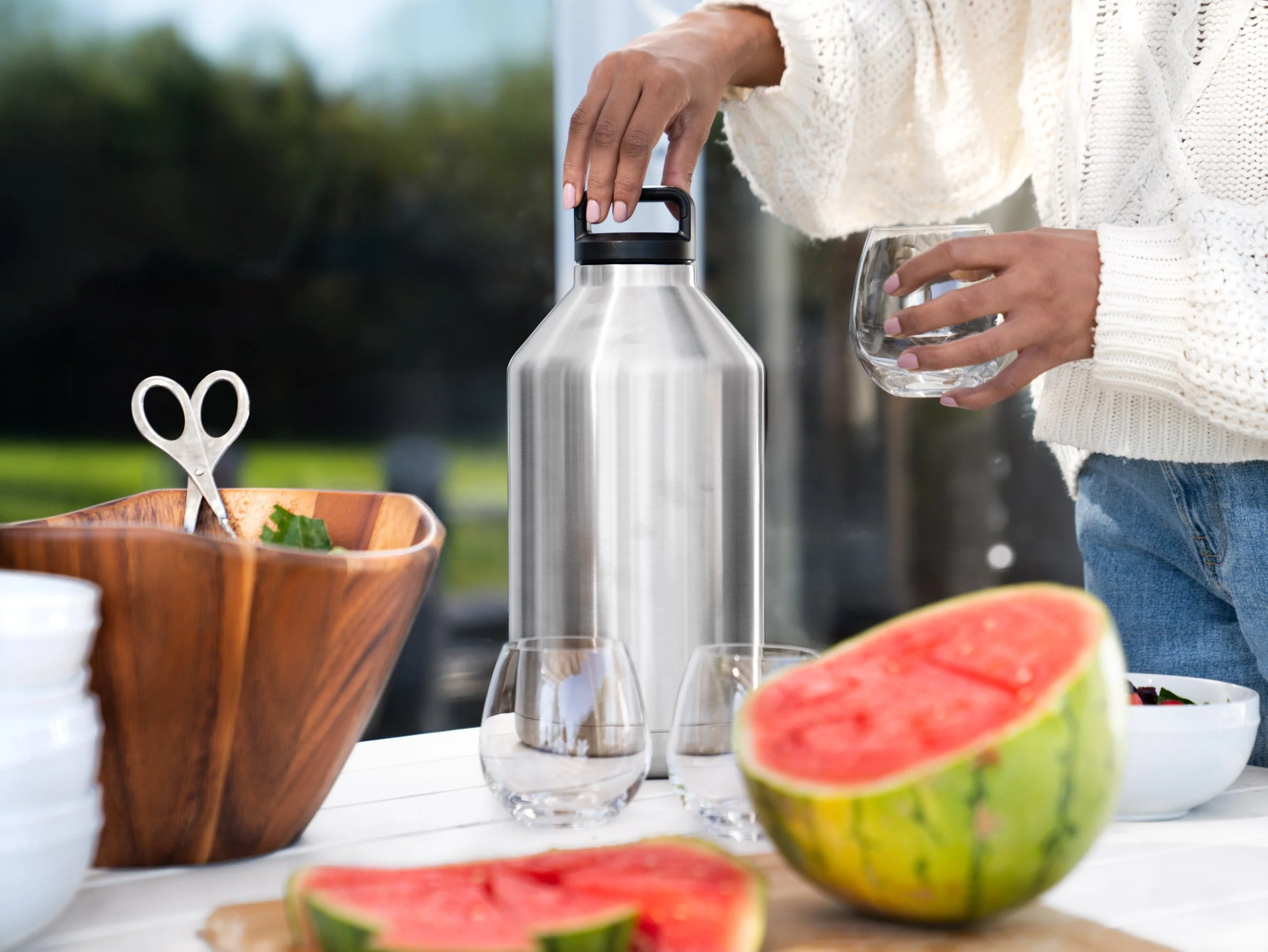 Reusable hydration bottle photographed in an outdoor lifestyle setting with a model pouring water, using soft natural light and clean composition for ecommerce use
