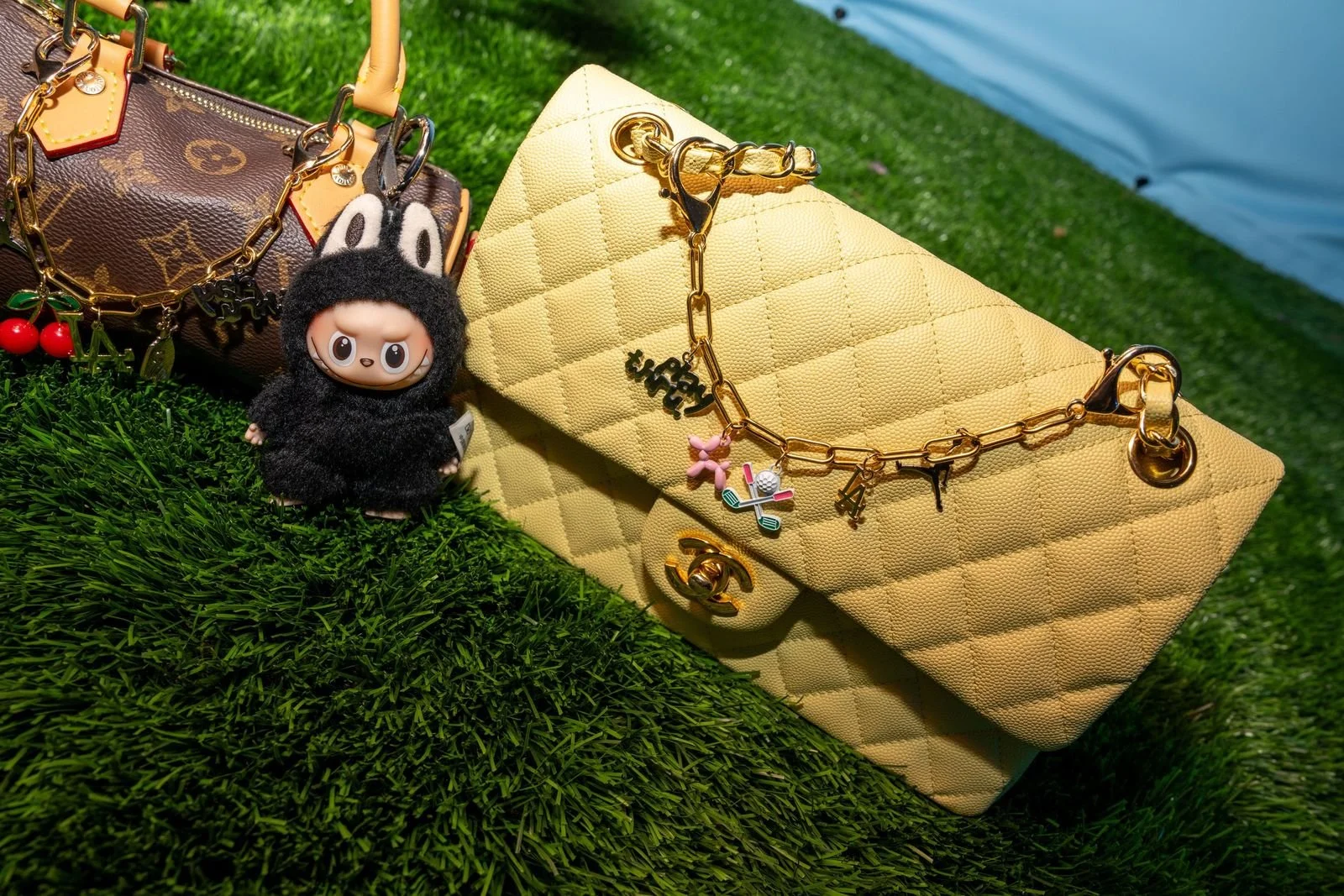 Luxury handbags and golf-themed charm accessories arranged on artificial turf at the Nike x Swang Golf event in Los Angeles