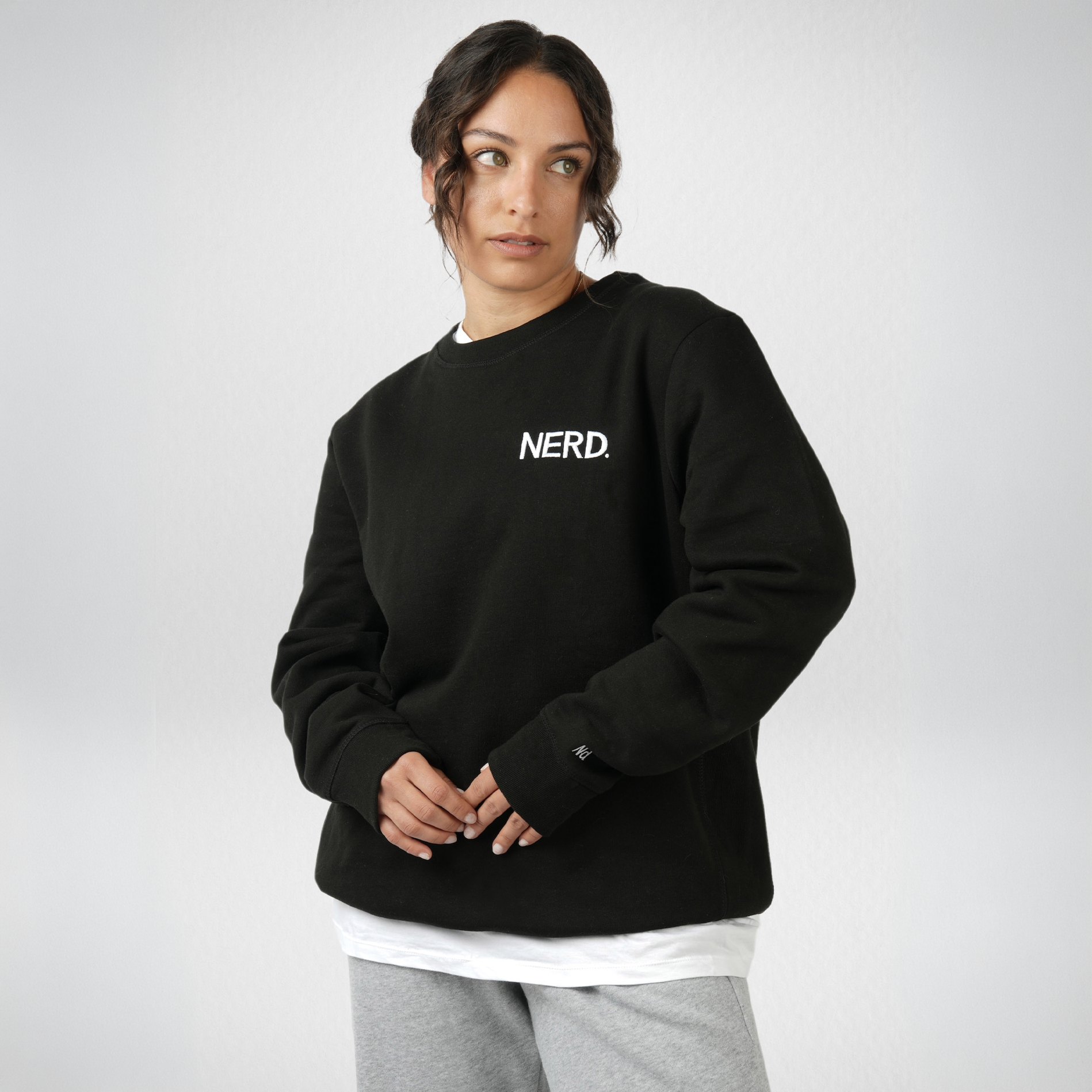 Female model wearing a black NERD sweatshirt photographed against a clean white studio background