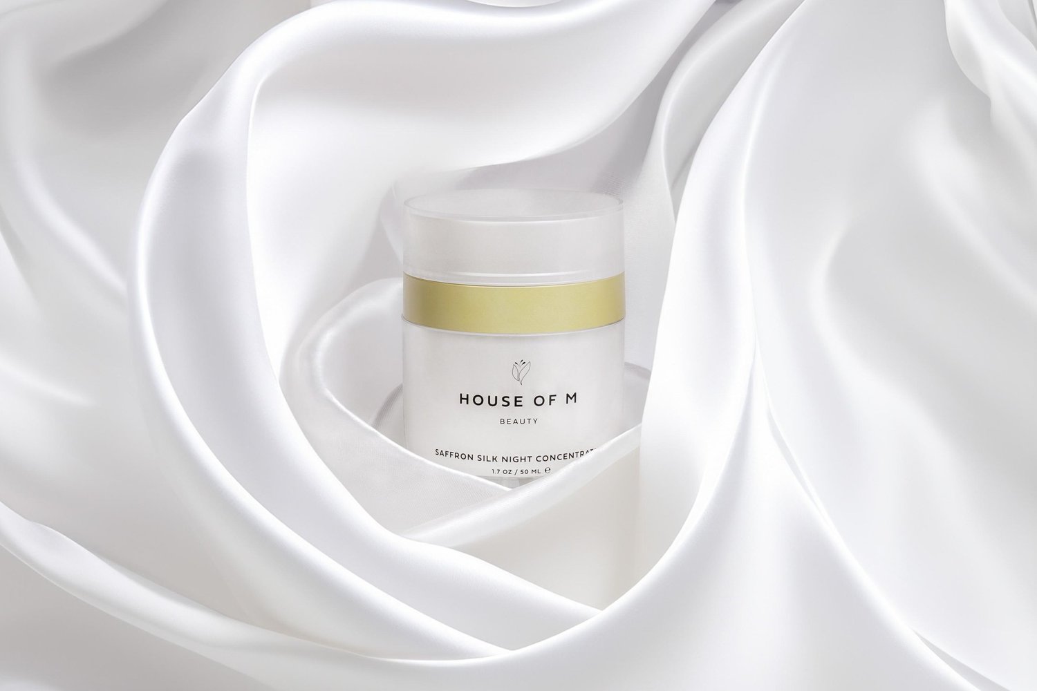 Luxury skincare product photography for House of M, jar and dropper styled on flowing silk fabric with soft directional studio light for a premium, elevated ecommerce presentation