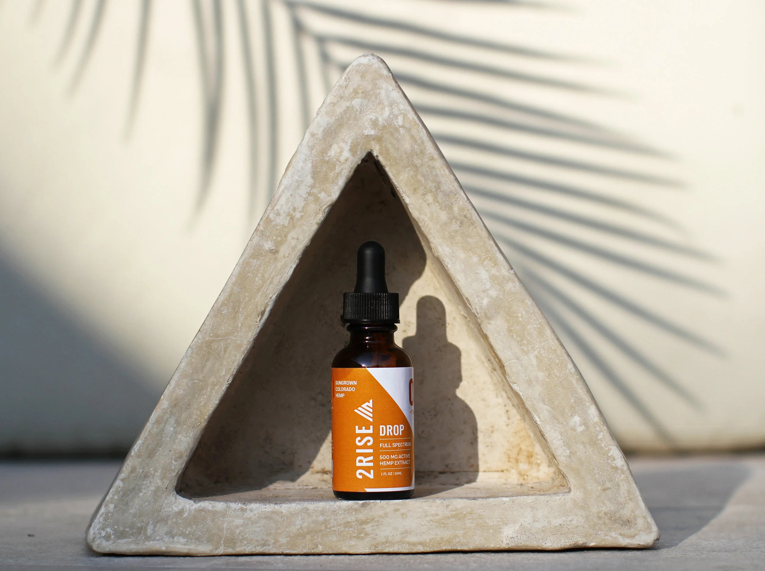 2Rise Drop bottle photographed inside a geometric concrete setup with hard directional sunlight and clean shadow lines for a modern ecommerce composition