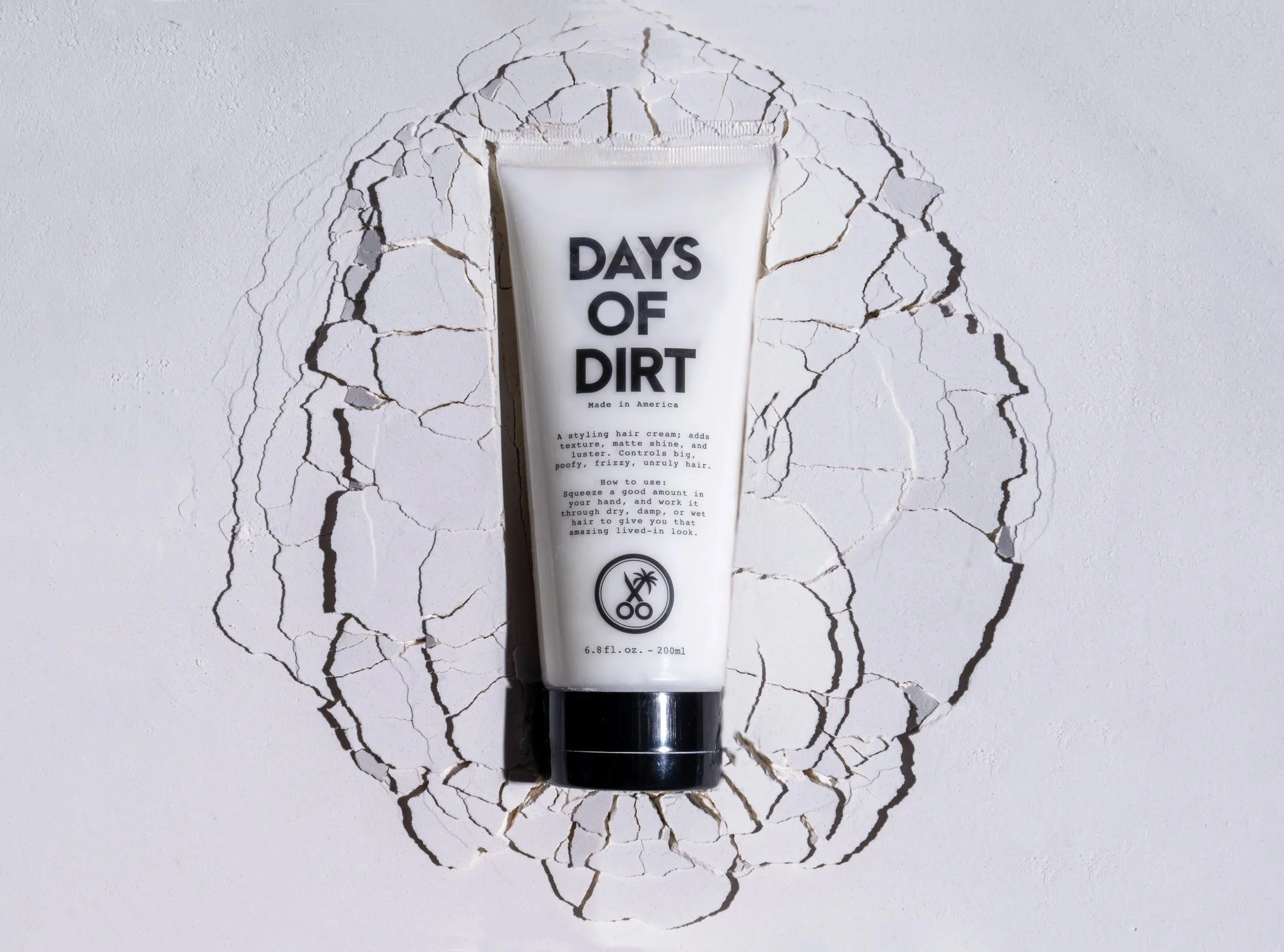 Days of Dirt hair product tube on a cracked white plaster surface, men's grooming product photography