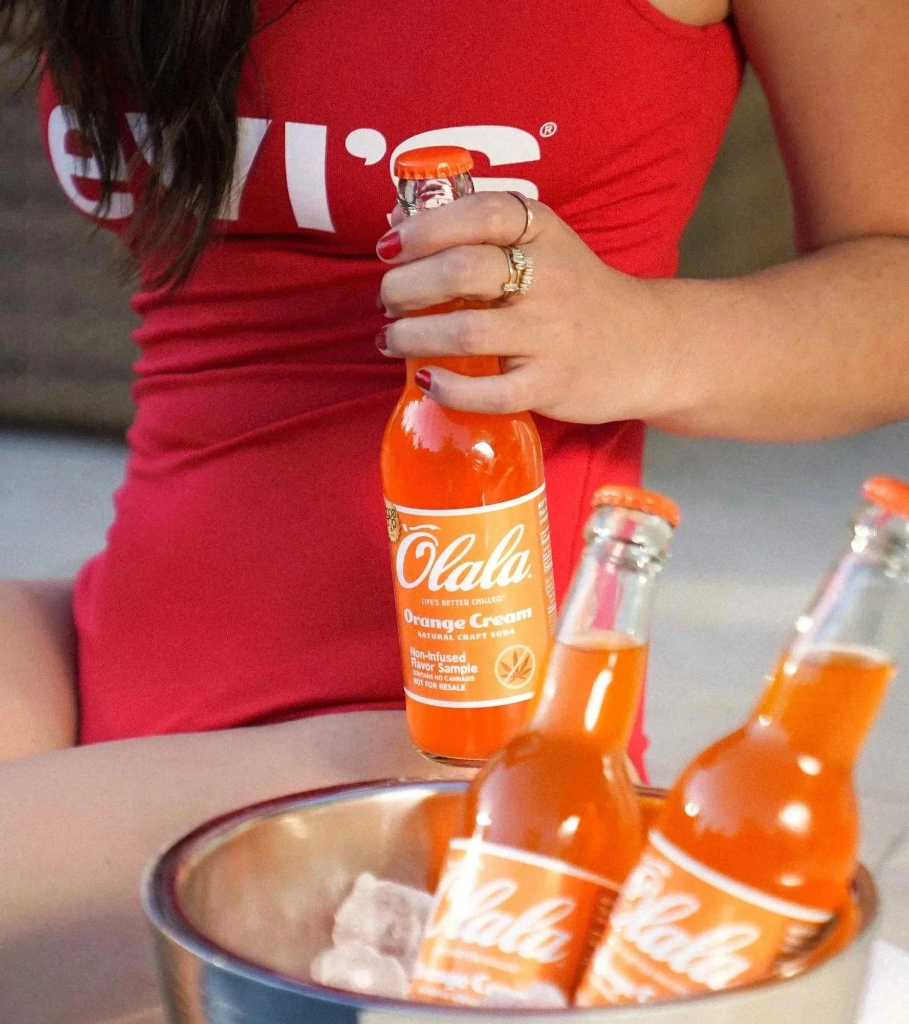 Model in a red Levi's top holding Olala orange soda bottles over an ice bucket