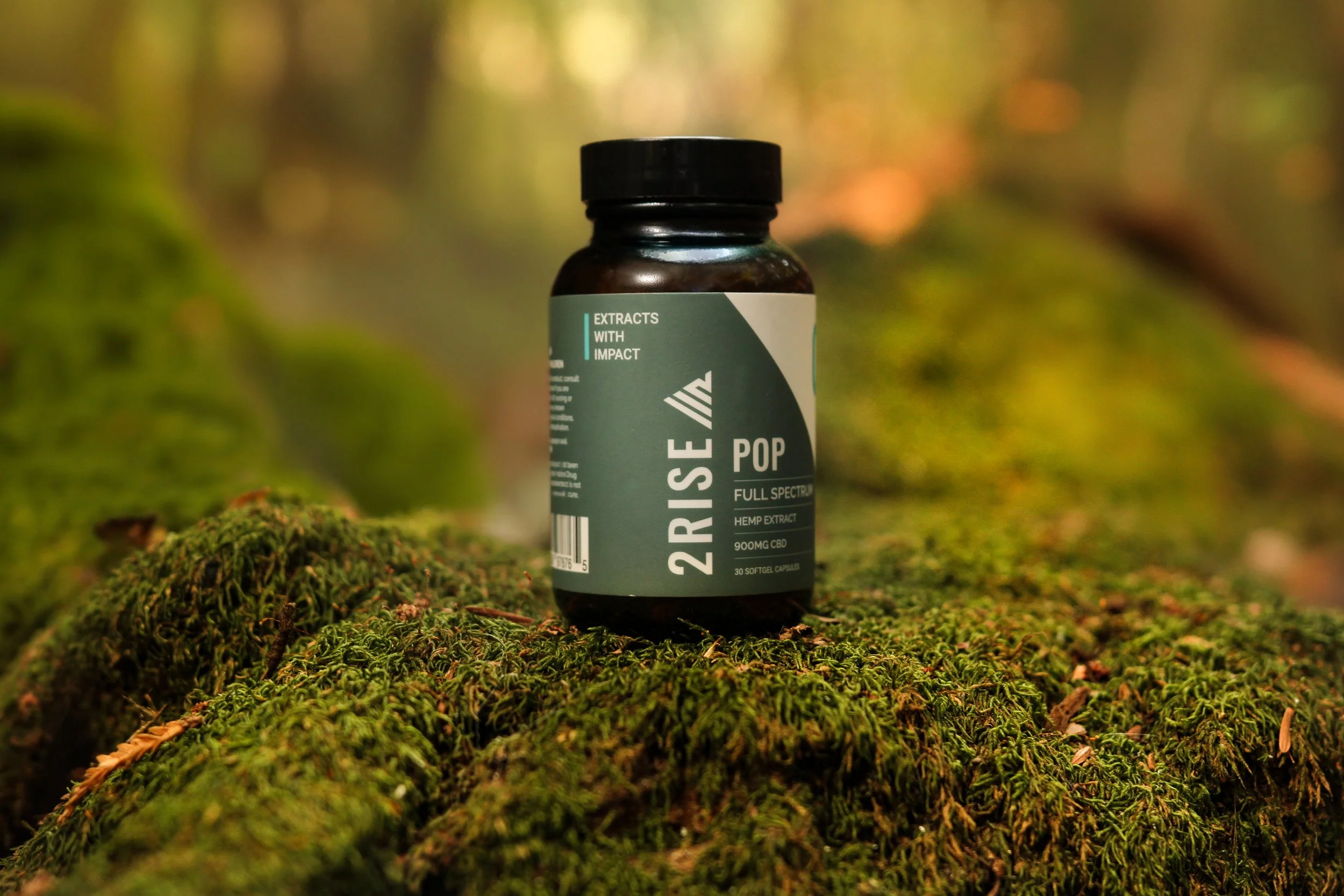 2Rise Pop supplement bottle photographed on moss in warm directional light, with shallow depth of field and a natural earthy mood for ecommerce imagery