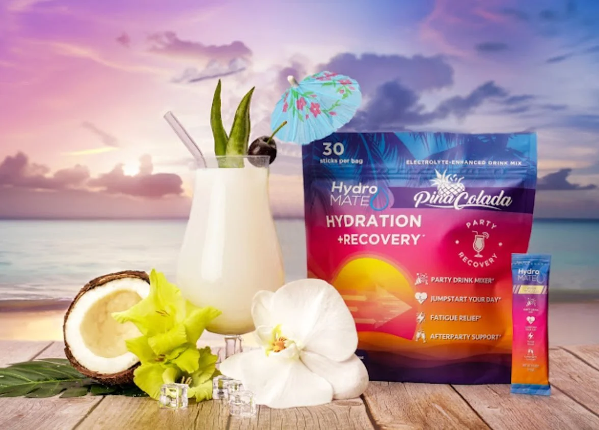HydroMate Pina Colada packaging styled with a tropical drink against a colorful sunset scene, ecommerce product photography