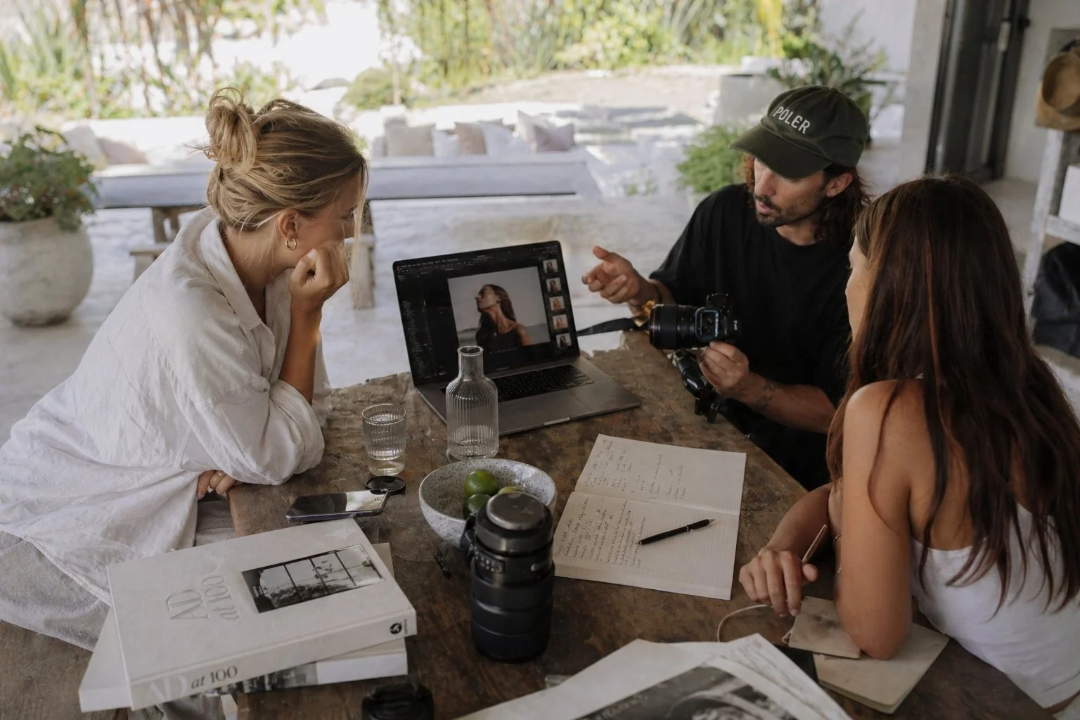 Photographer reviewing shots on a laptop with two clients at an outdoor table during a commercial photo shoot