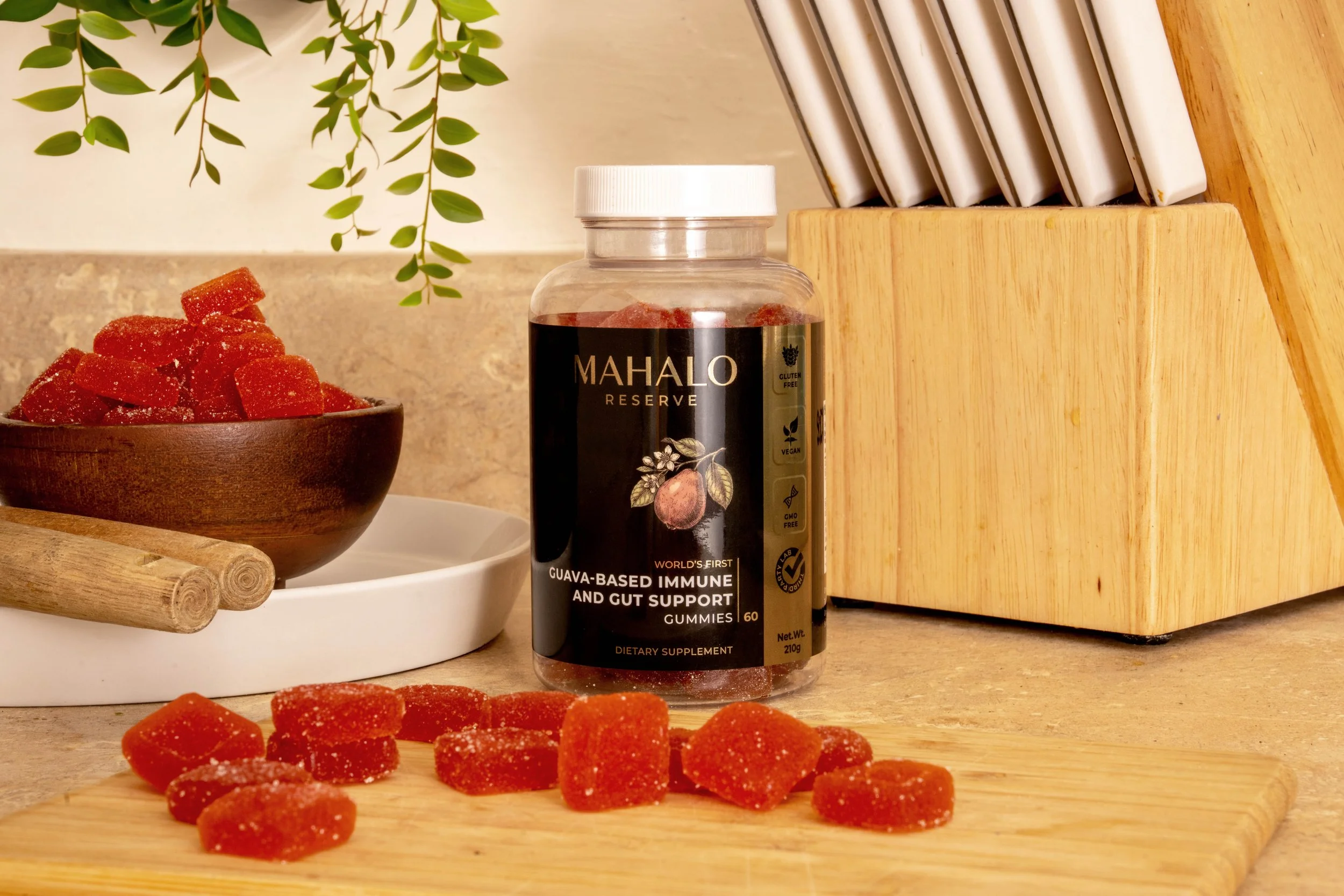 Mahalo Reserve supplement gummies photographed in a warm kitchen still life, using directional window-style light, natural wood textures and scattered gummies to define the bottle shape, label detail and amber product color.