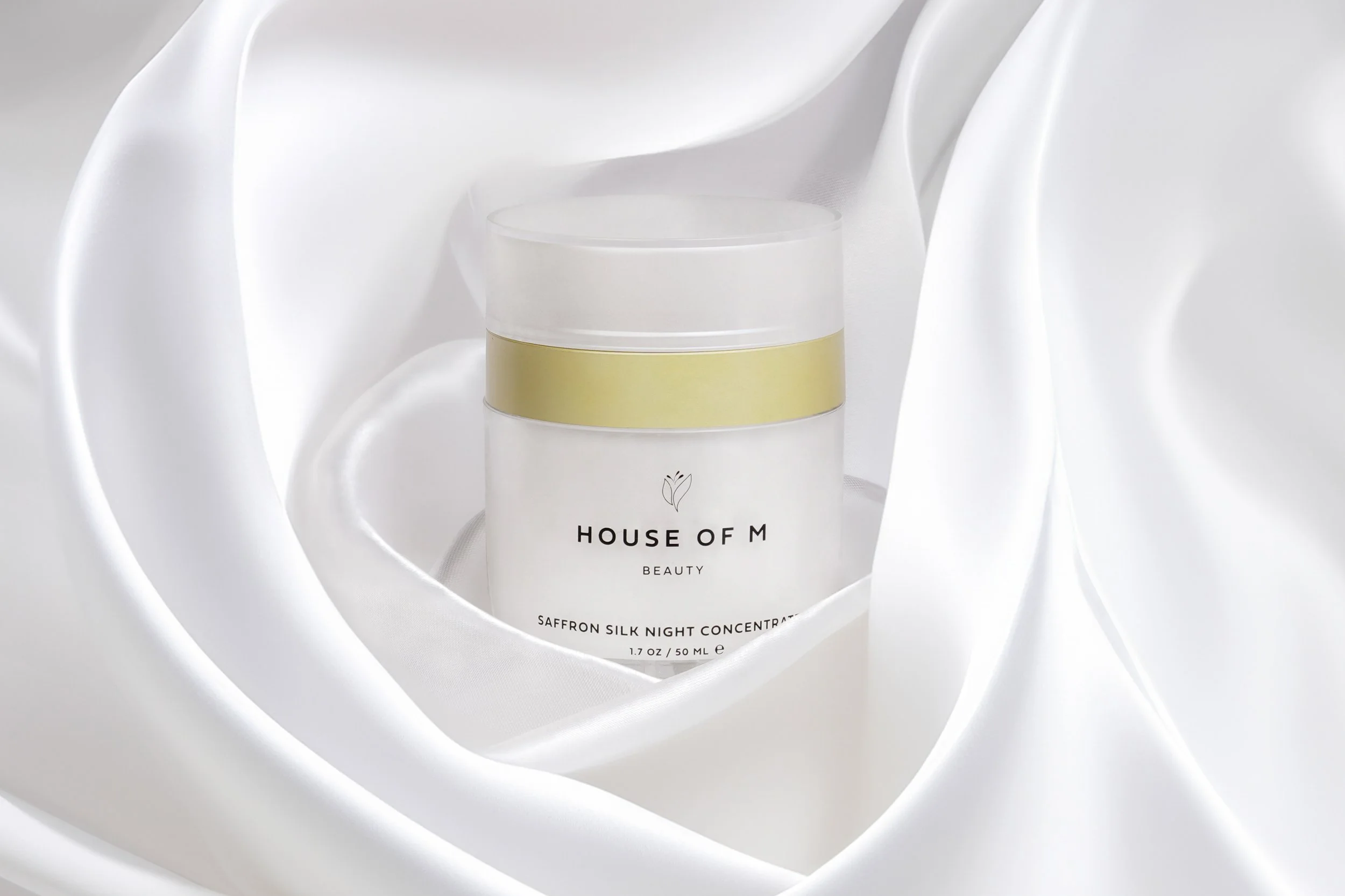 House of M Beauty skincare jar photographed on draped white satin with soft studio lighting