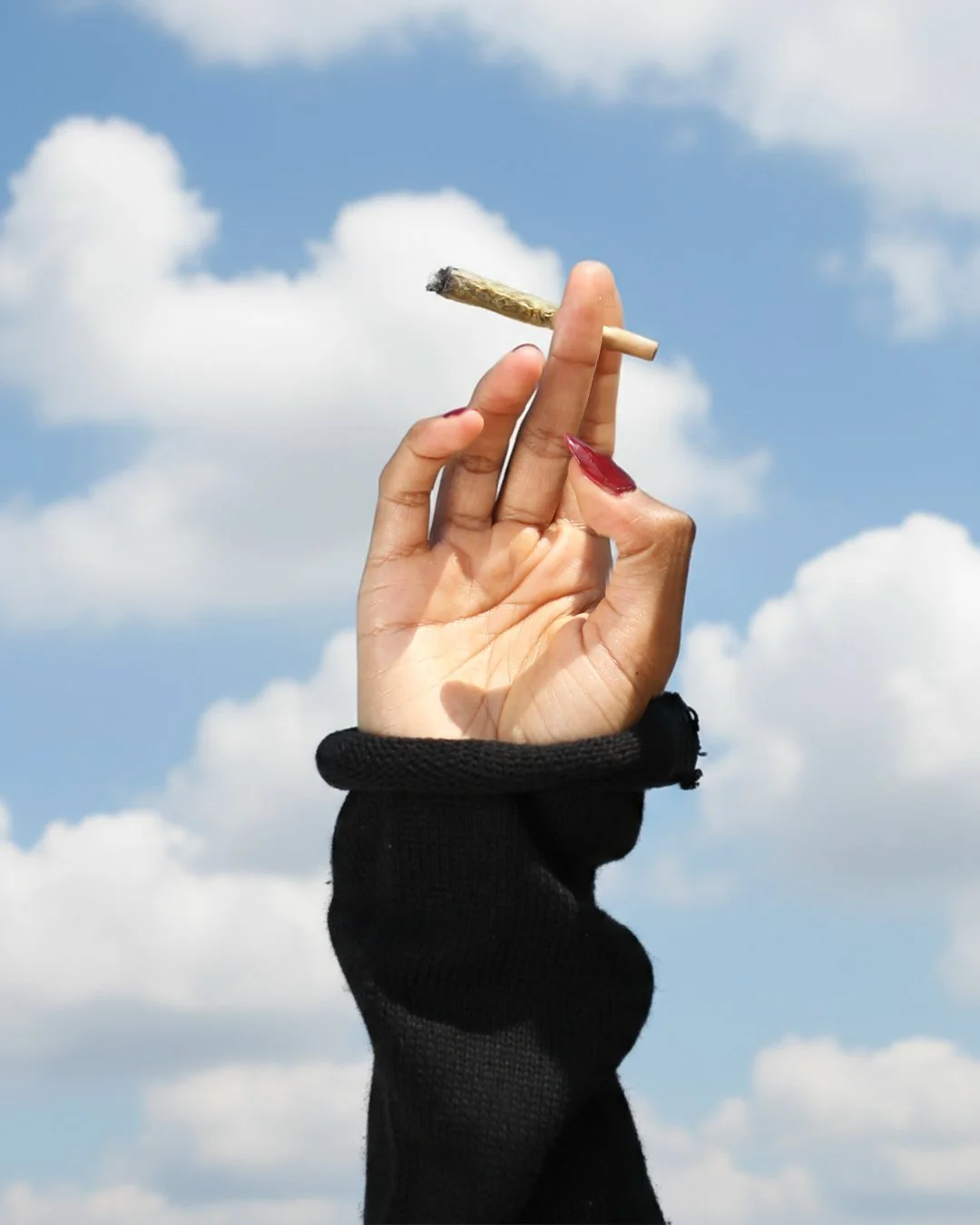 California pre-roll lifestyle photography with hand holding cannabis joint against blue sky