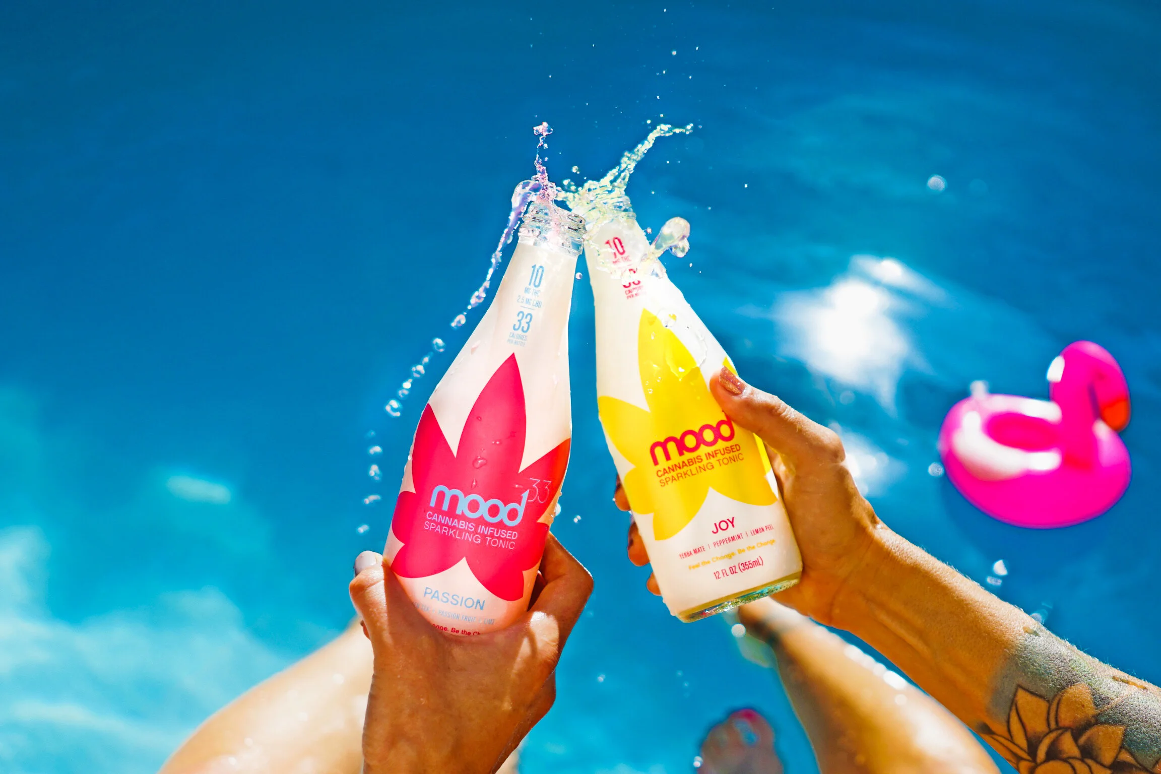 Lifestyle product photography, hands clinking bottled drinks with splash on blue